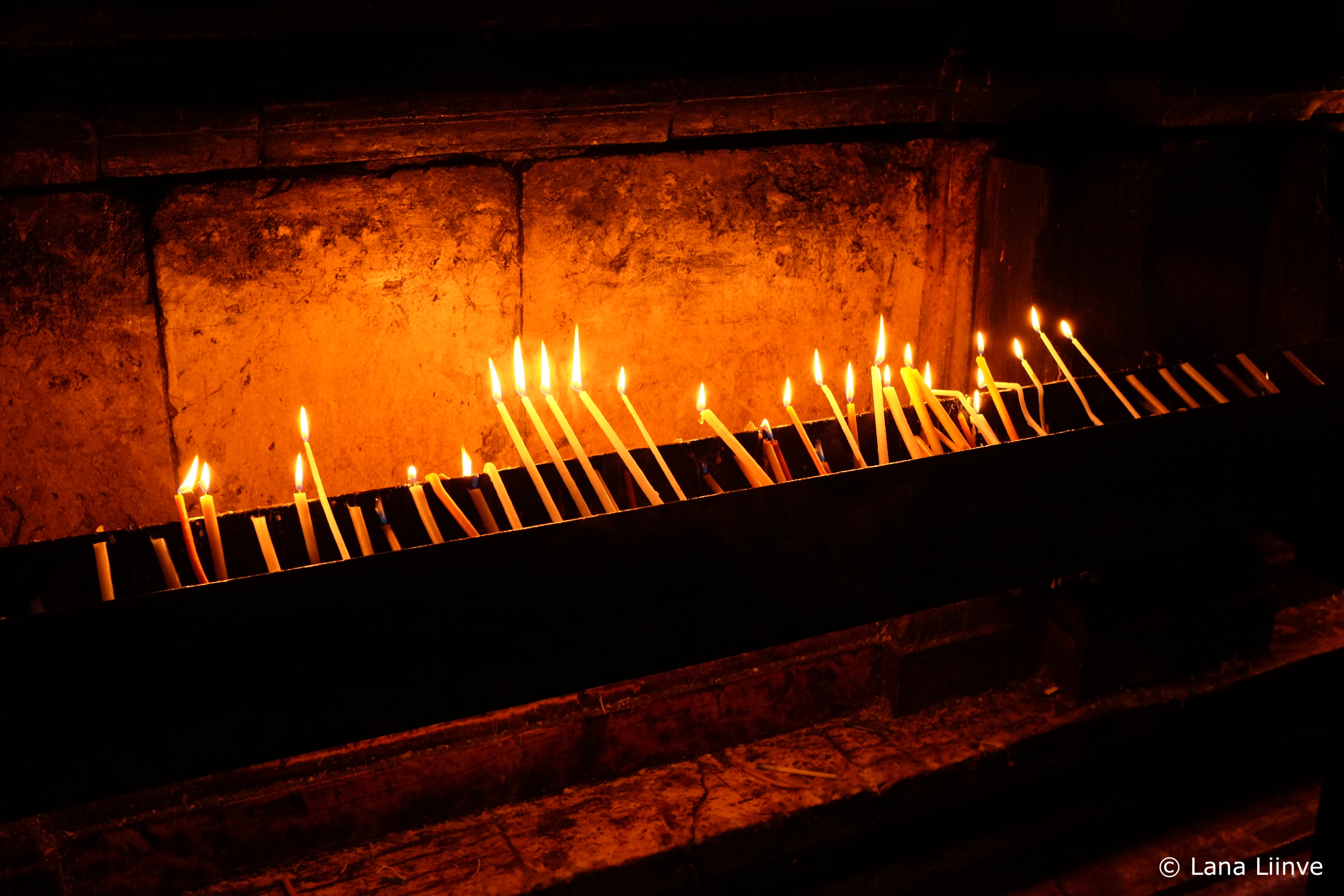 A photo of numerous thin, lit prayer candles inside the Church of the Holy Sepulchre in Jerusalem
