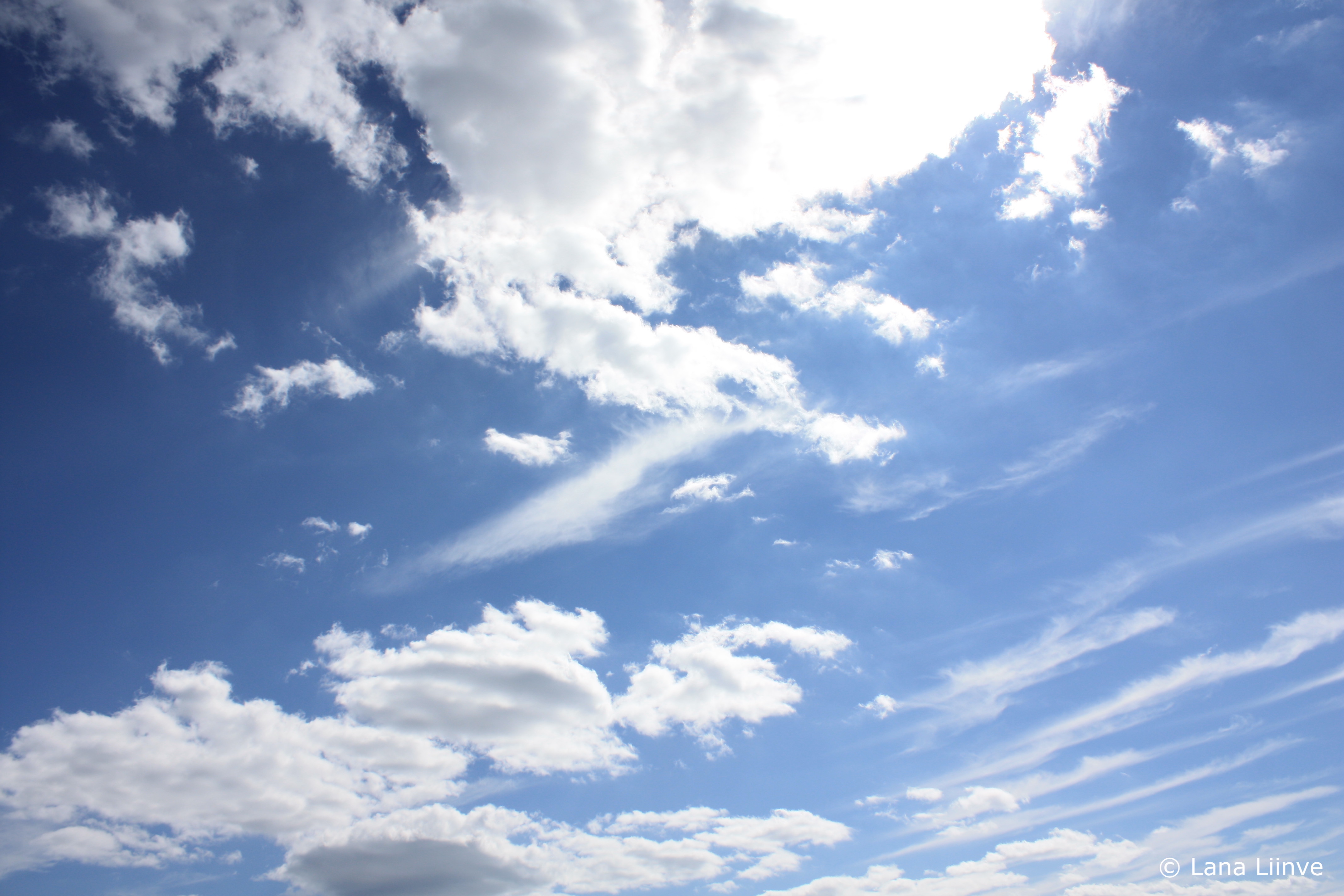 A photo of a bright, blue sky on a sunny day with scattered streaky and fluffy white clouds