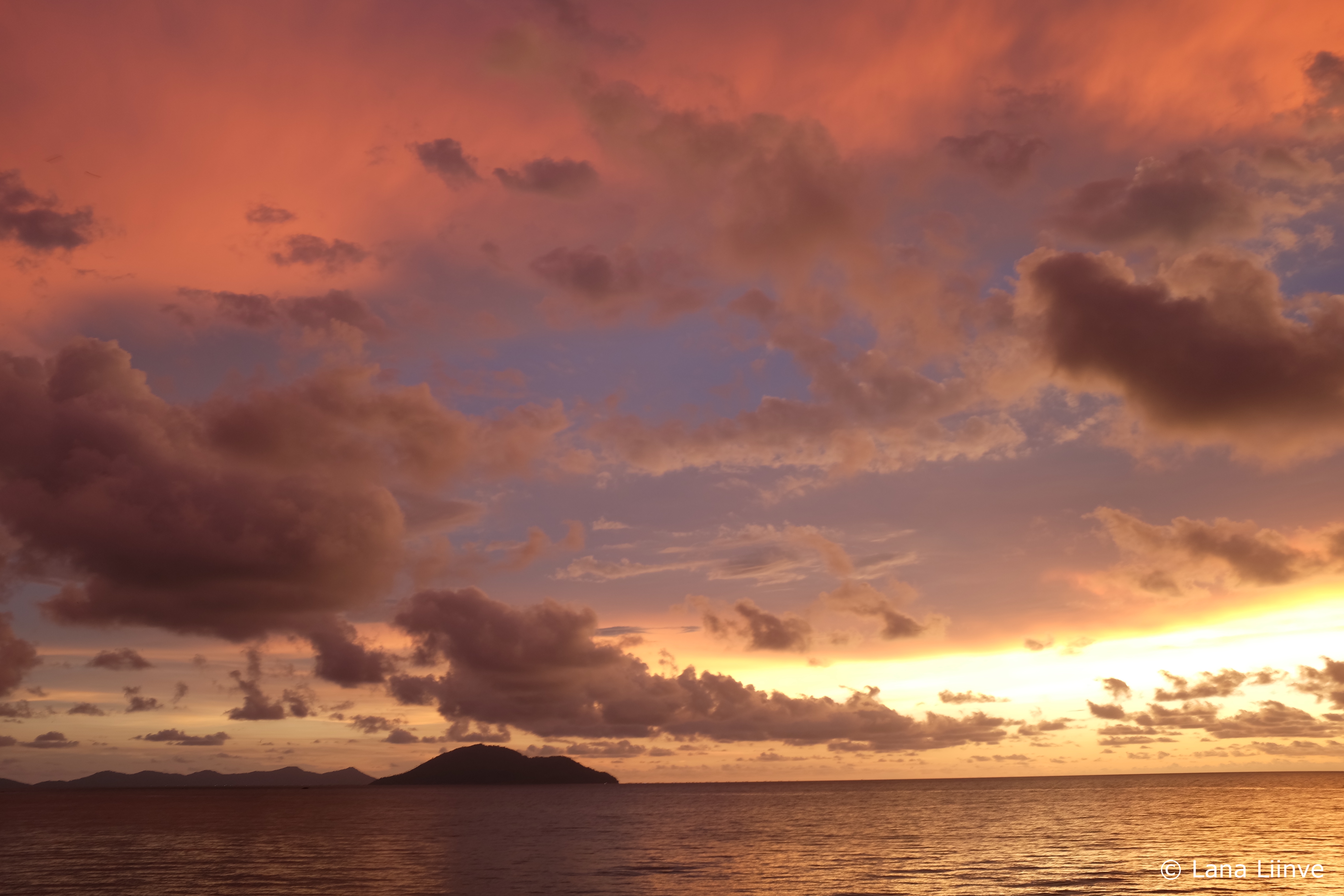 A photo of a bold pink, blue, and yellow sky with fluffy clouds at sunset in Kalimantan, Borneo