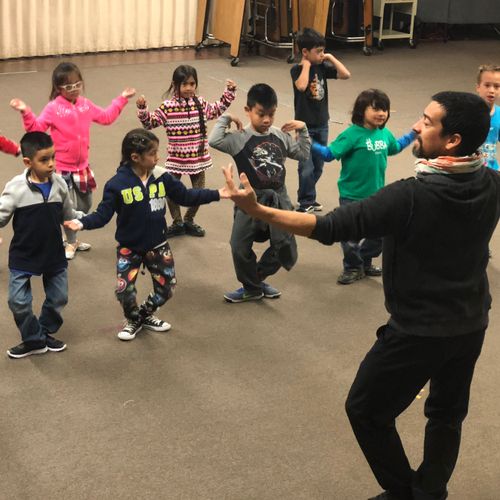 A male ballet instructor teaching several young children with regular street clothes.