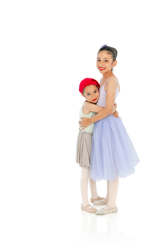 Two young girls hugging and wearing ballet attire