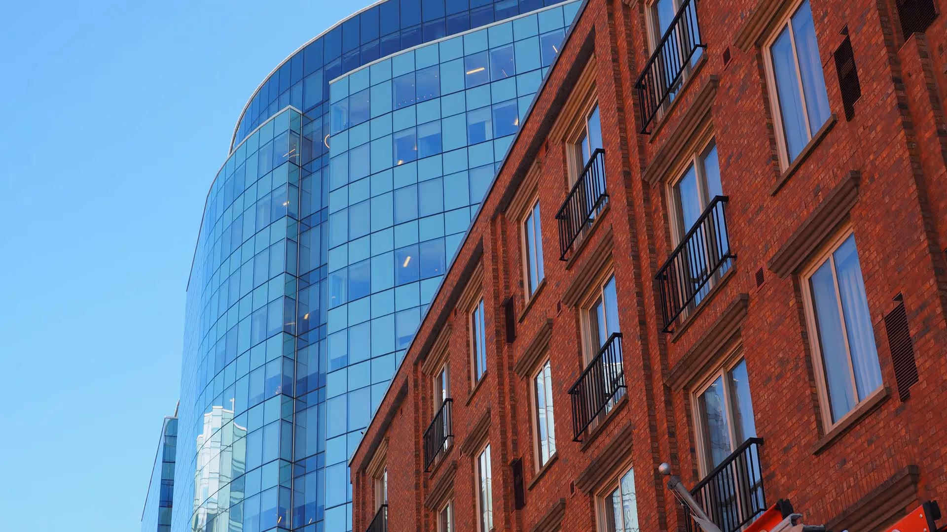 A modern glass building stands beside an older brick building under a clear blue sky.