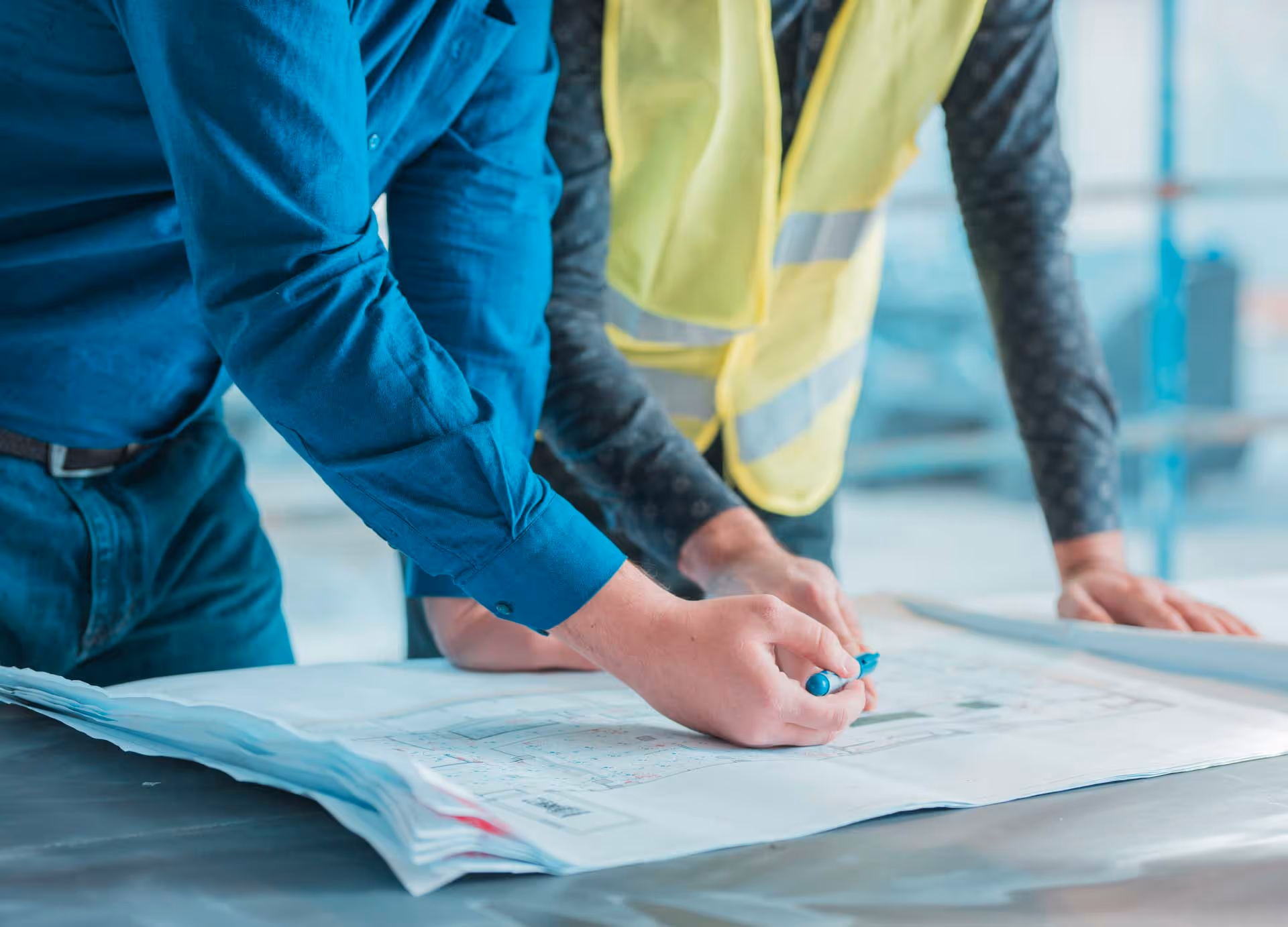 Two people study architectural blueprints on a table.