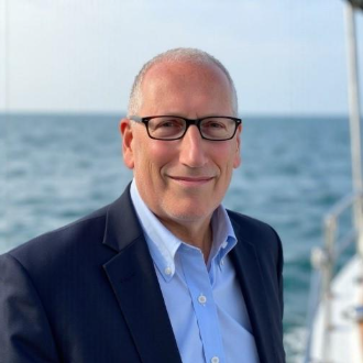 A person in a suit and glasses smilingAI-generated content may be incorrect.