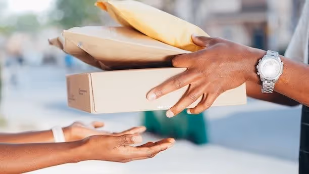 A pair of hands delivering a cardboard box and padded envelopes to another pair of hands.