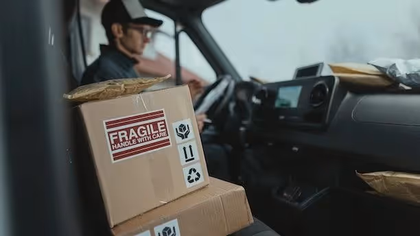 A delivery driver in the cab of his truck with parcels stiing beside him.