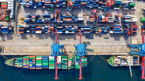Aerial view of a busy shipping port with cargo containers, cranes, and docked container ships.