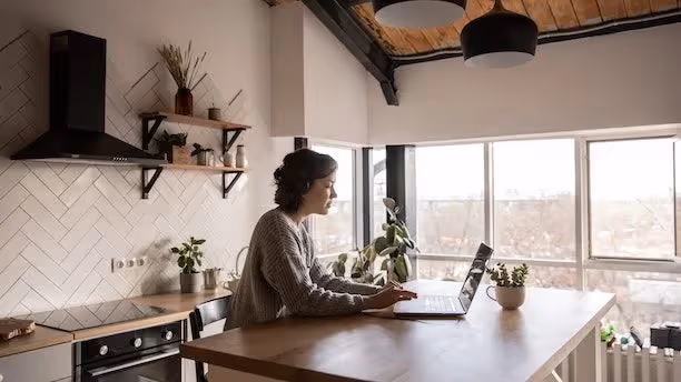 Woman working on a laptop at a kitchen counter in a bright modern home.