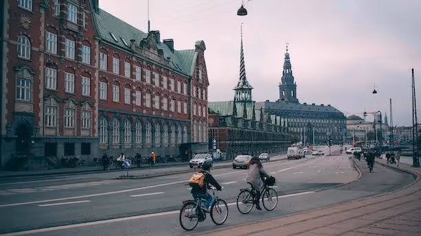Cyclists ride past historic buildings in Copenhagen, including the Old Stock Exchange and Christiansborg Palace.