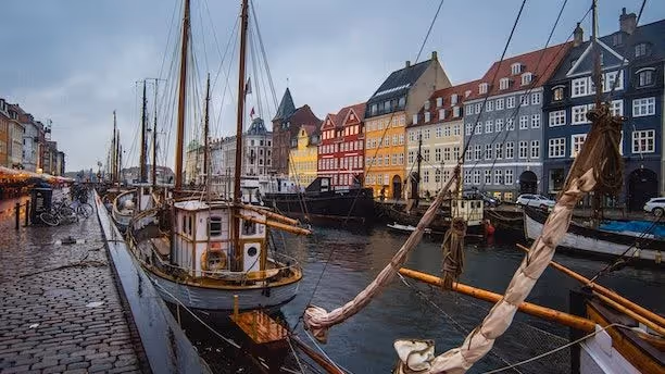 Colorful townhouses line the canal in Nyhavn, Copenhagen, with wooden sailing boats moored along the quay.