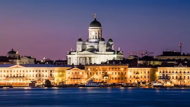 Helsinki Cathedral lit up at night with waterfront buildings in front.