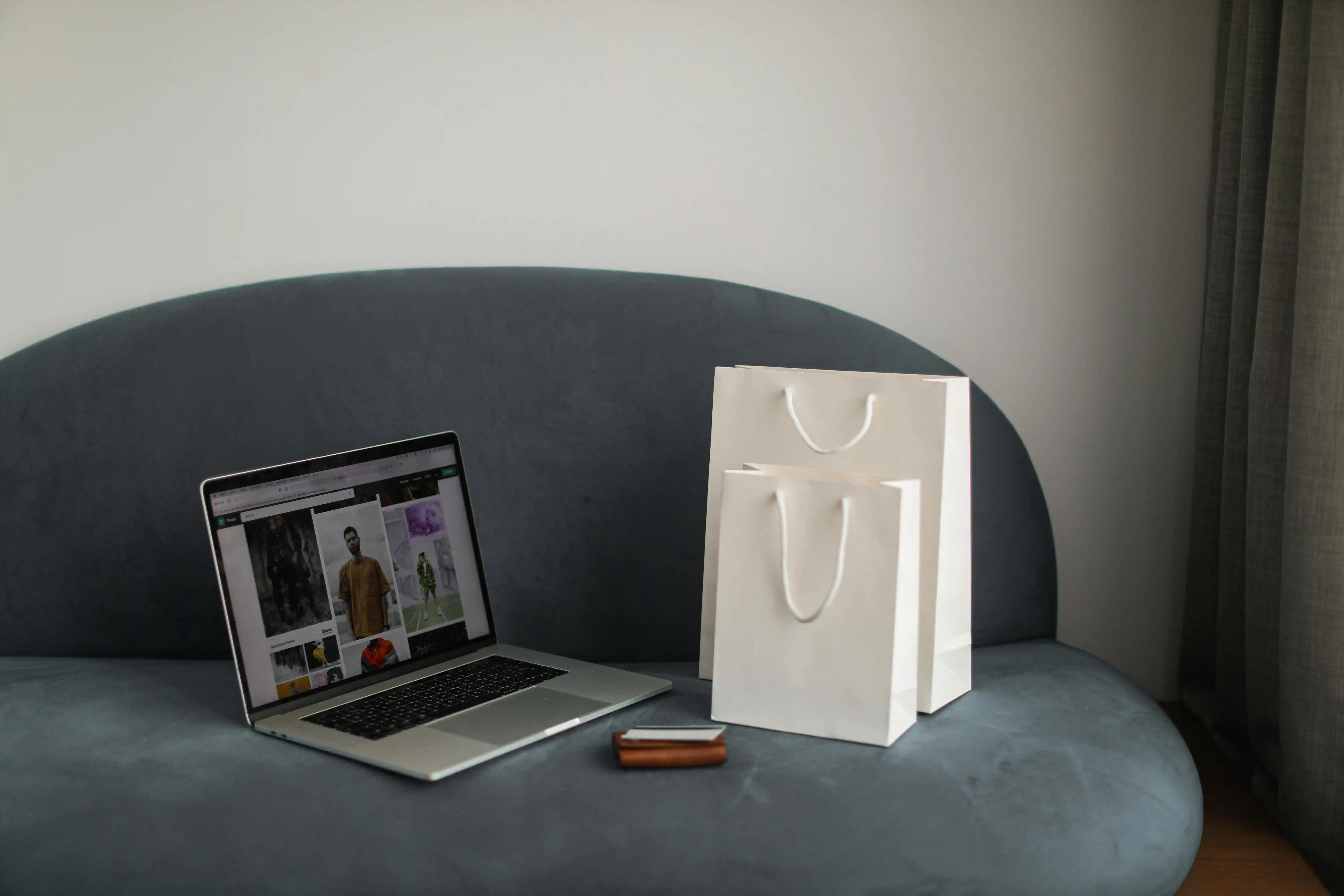 Laptop, wallet, and two white paper bags on a grey sofa.