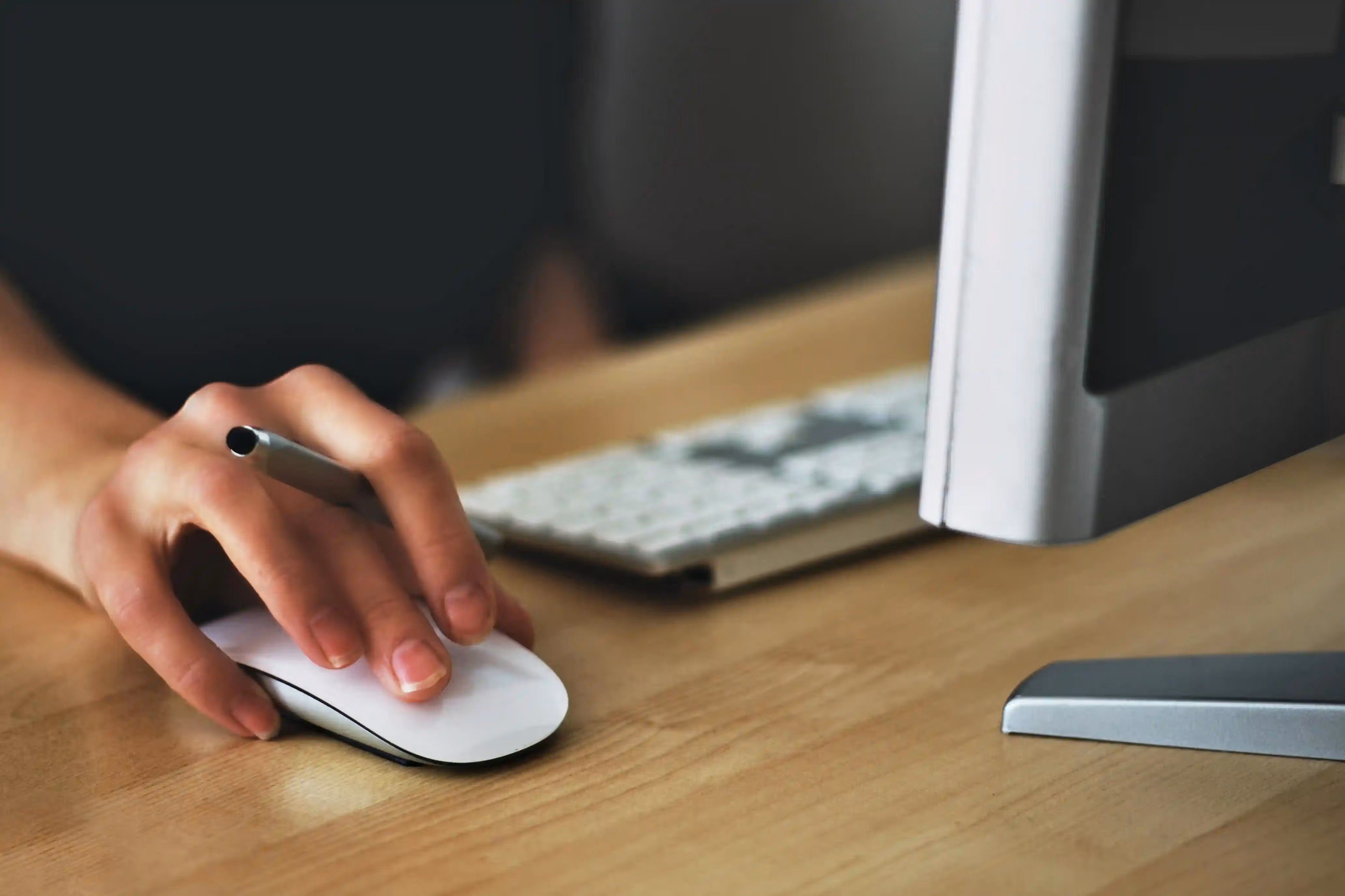 Person holding an apple mouse works on a desktop computer.