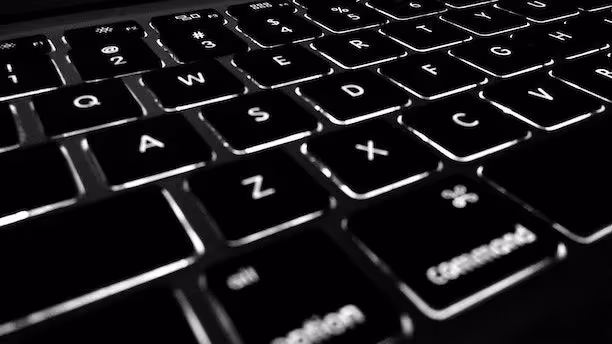 Close-up of a backlit computer keyboard in low light, showing illuminated keys.