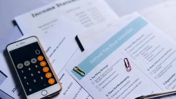 A tax preparation checklist, income statement, and a smartphone calculator on a desk.