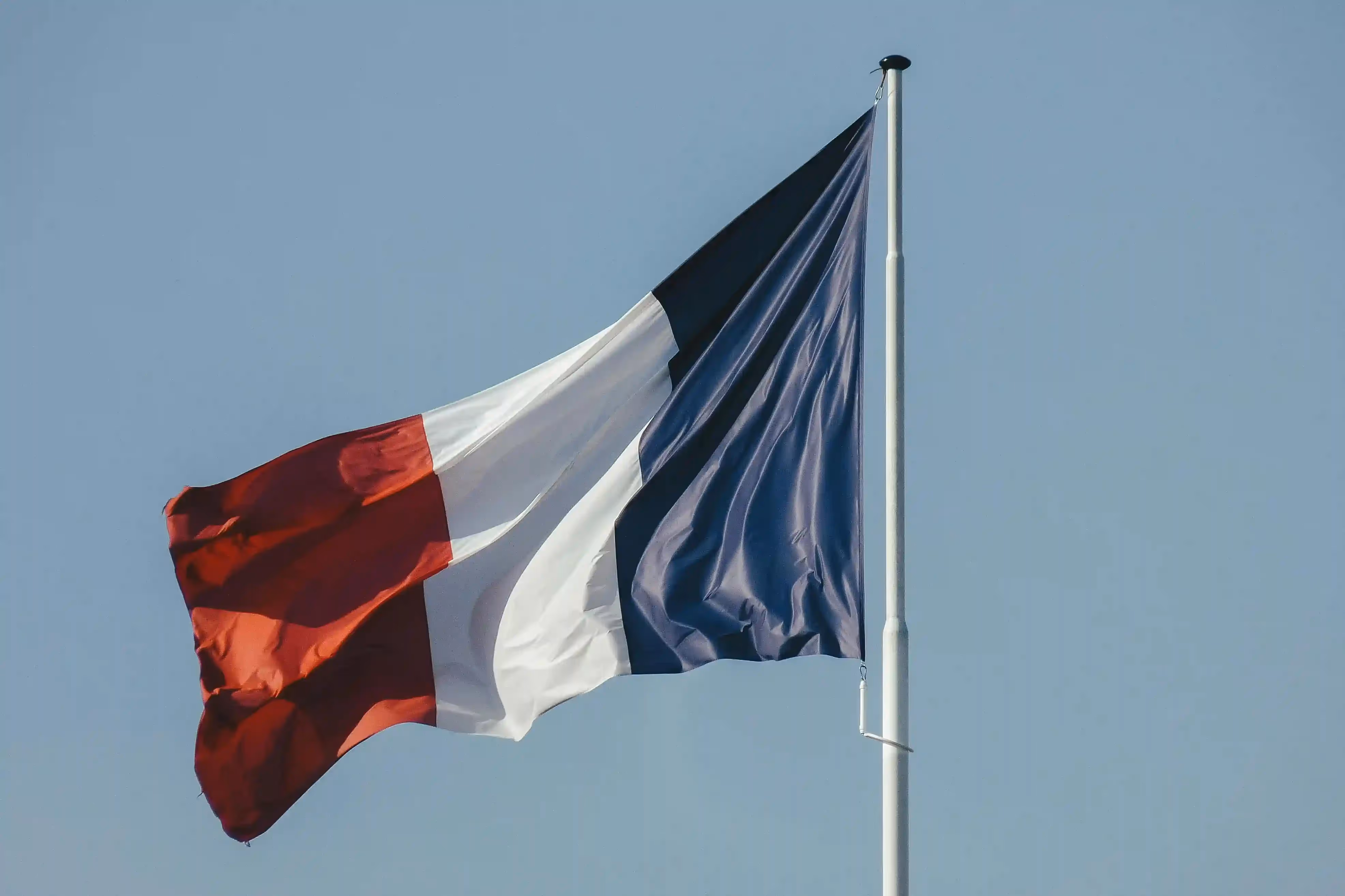 French flag waving against a clear blue sky, representing France's national identity.