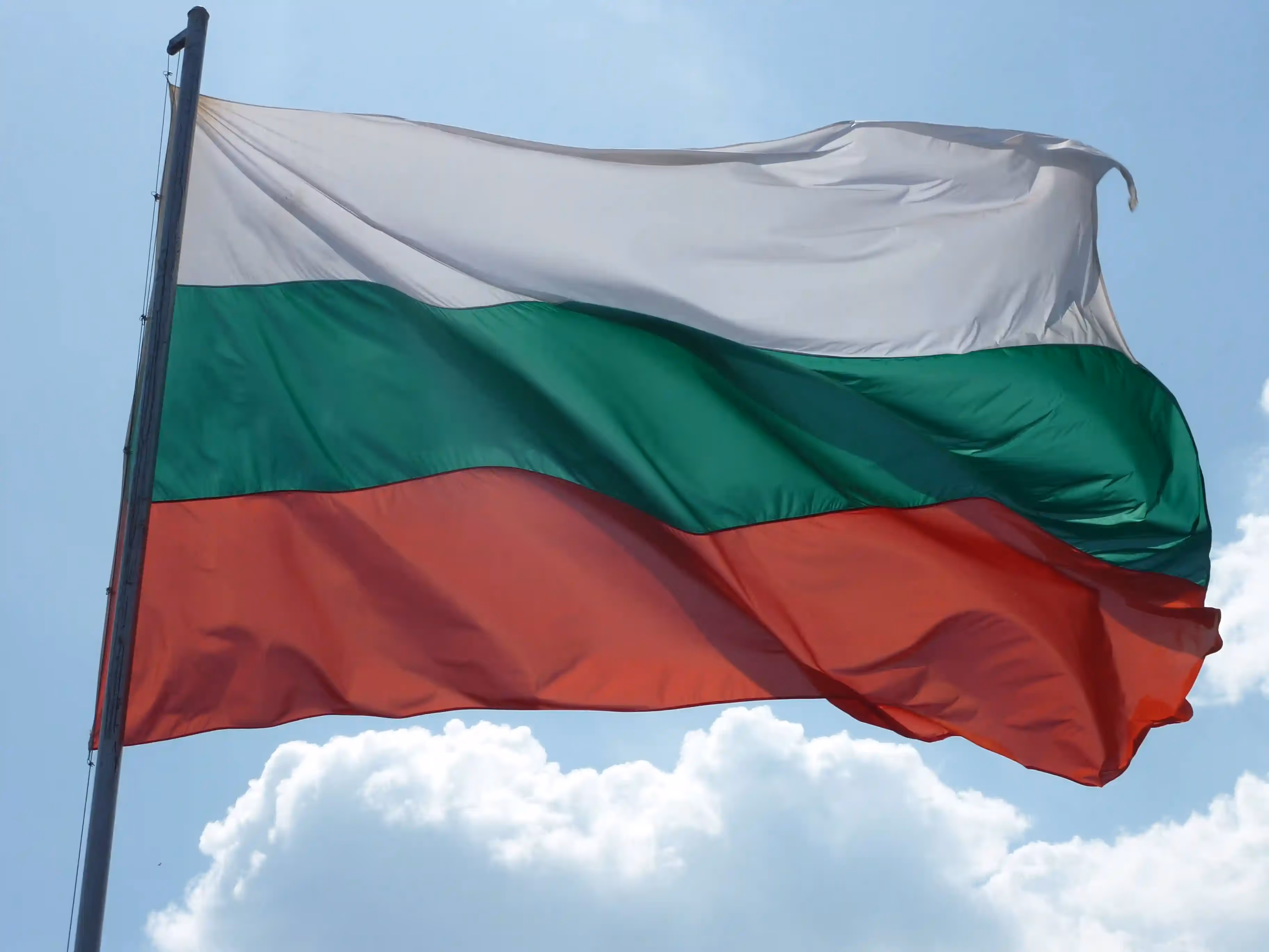 Bulgarian flag with white, green, and red stripes waving in the sky.