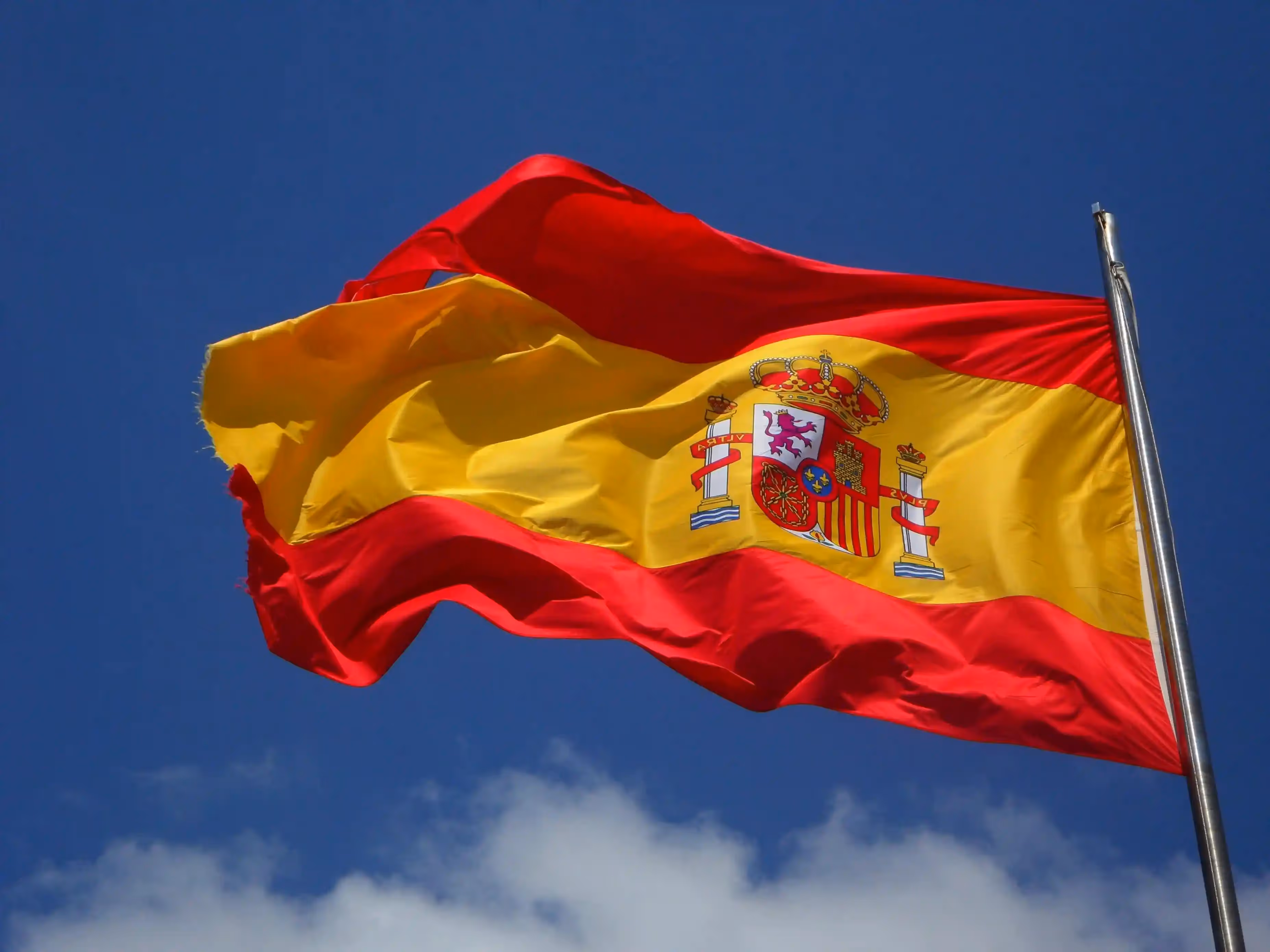 Spanish flag with red and yellow stripes and a coat of arms, waving in the sky.