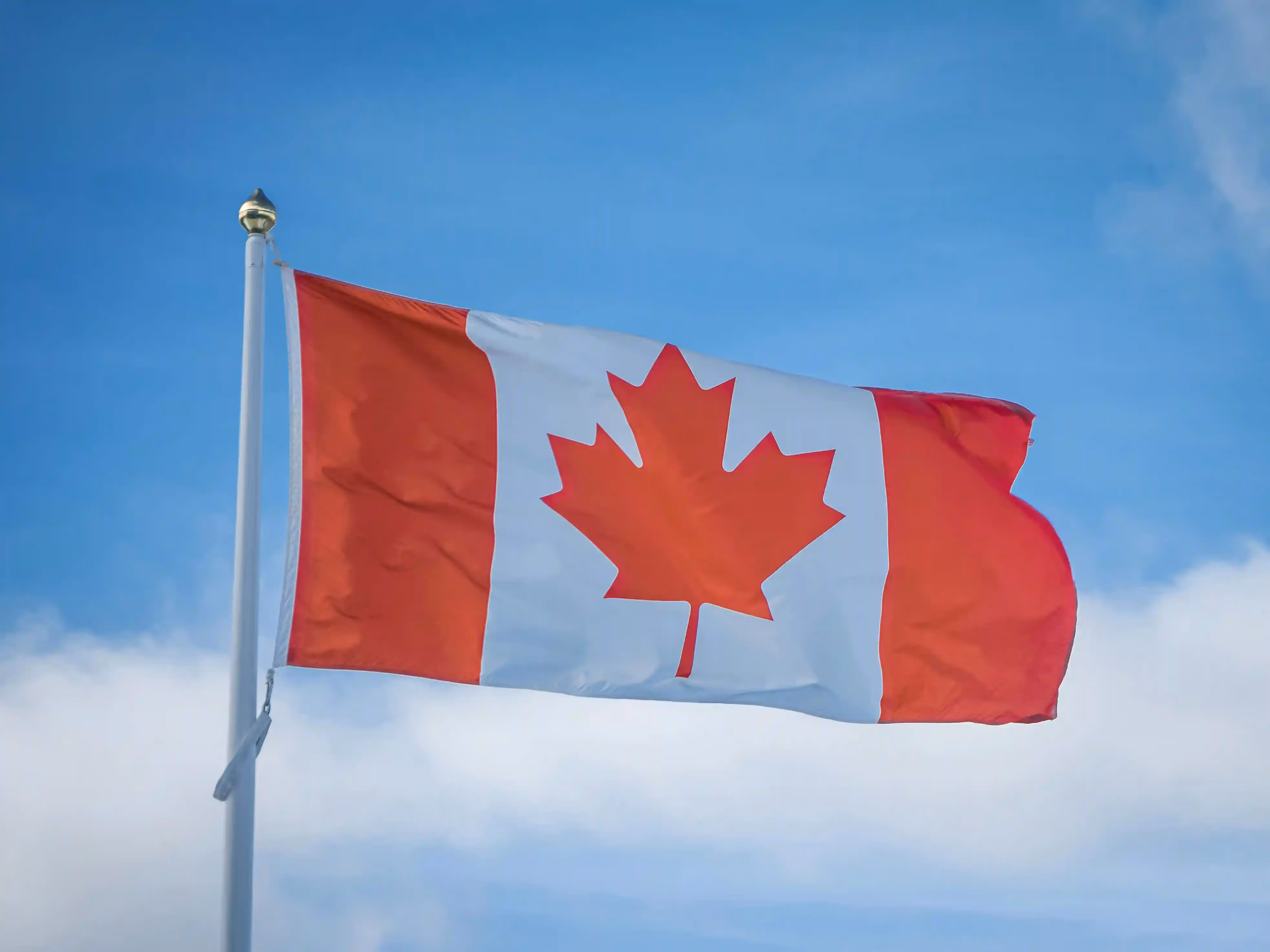 Canadian flag waving against a blue sky with clouds.