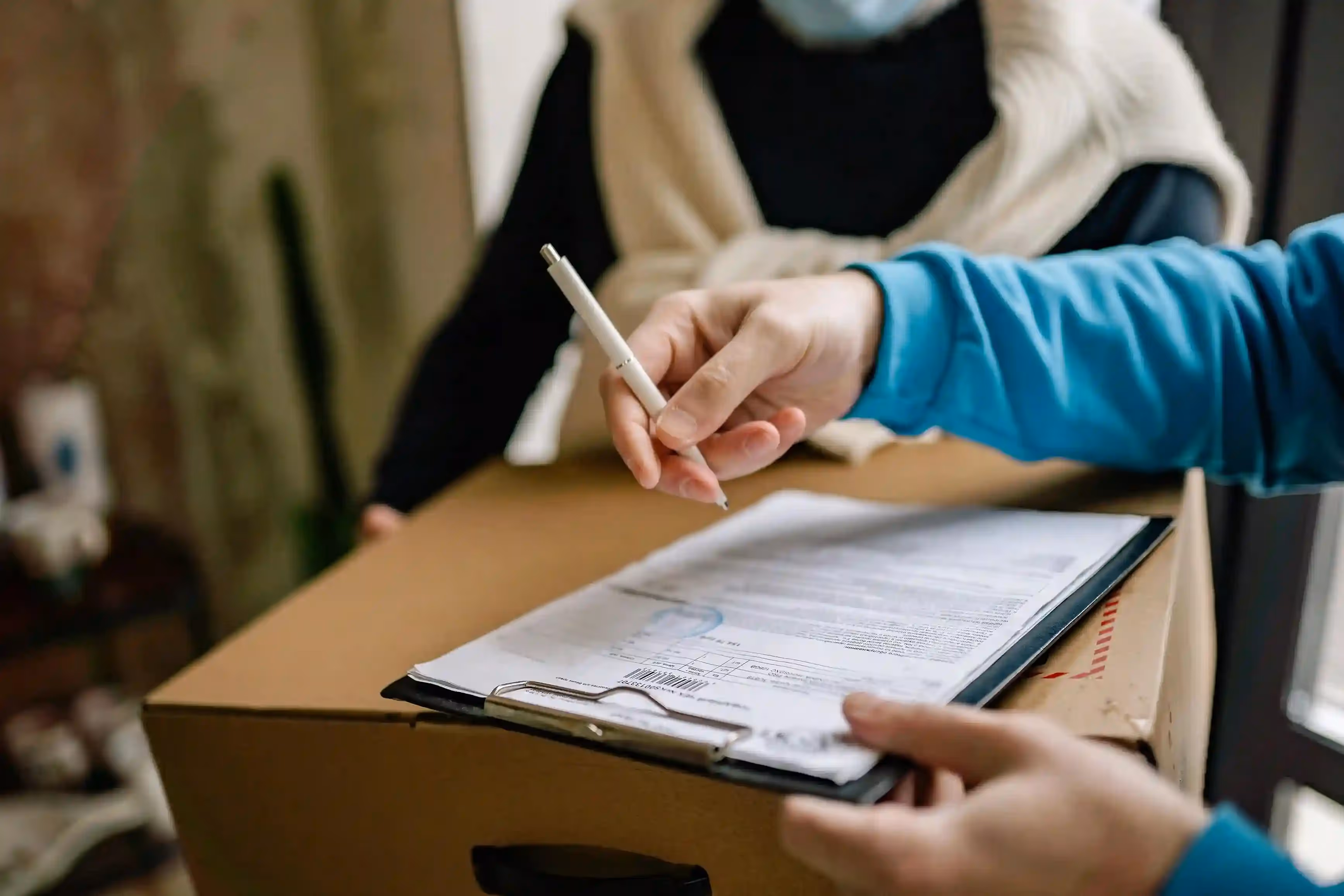 Person holding pen and clipboard on top of a cardboard box.