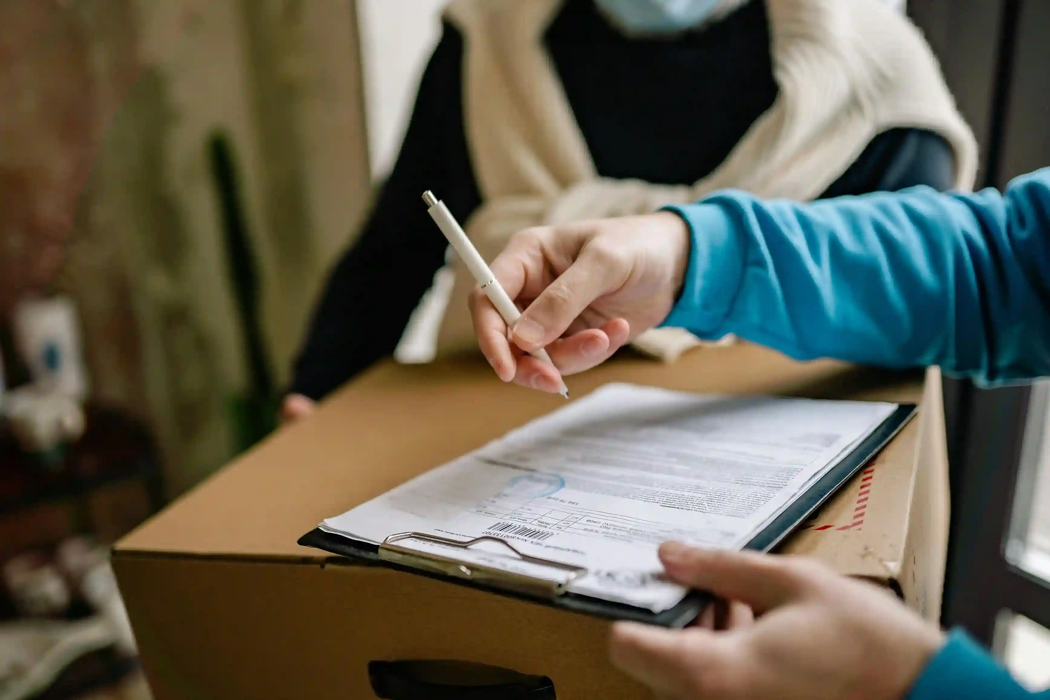 Person holding pen and clipboard on top of a cardboard box.