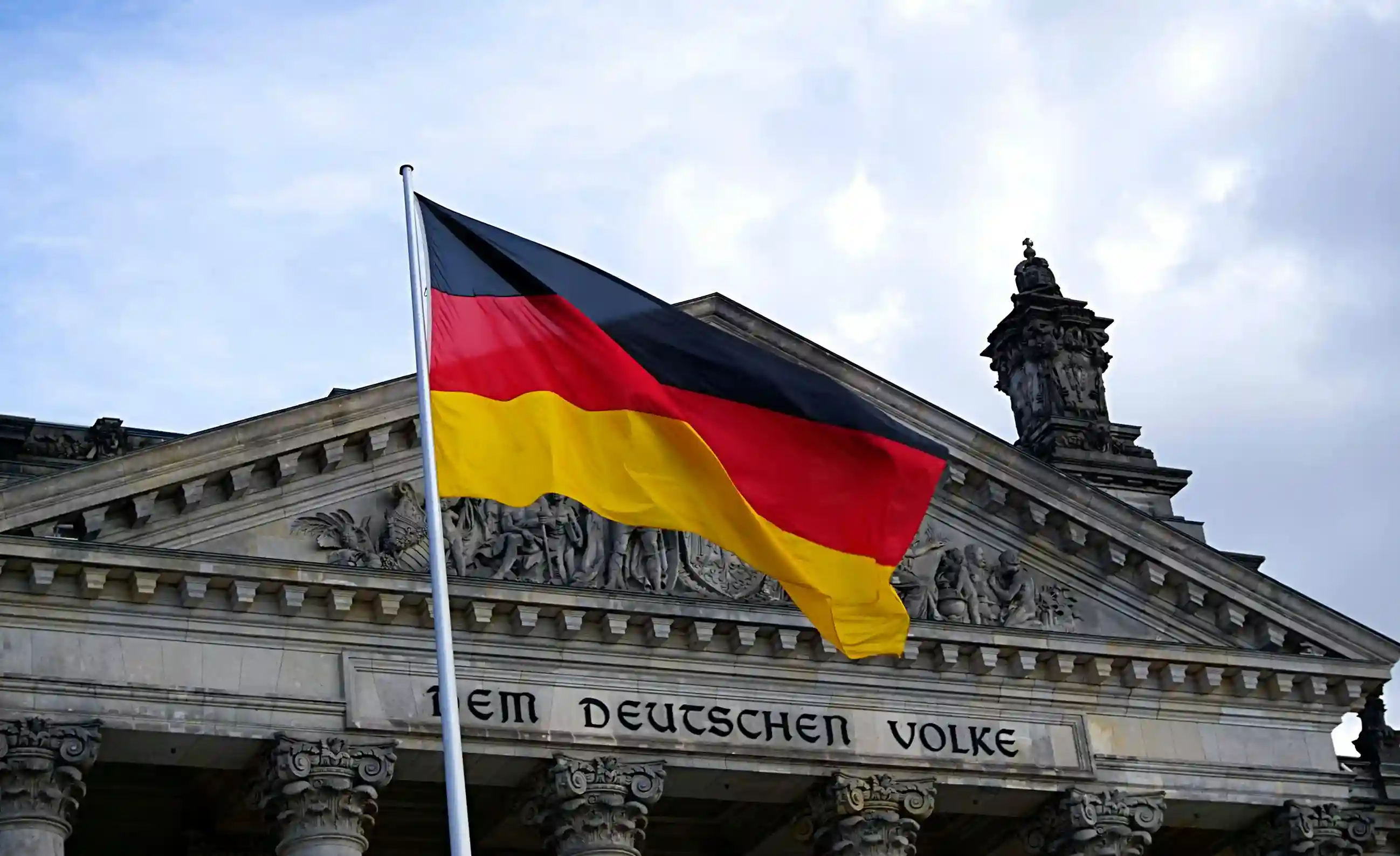 German flag waving in front of the historic Reichstag building in Berlin.