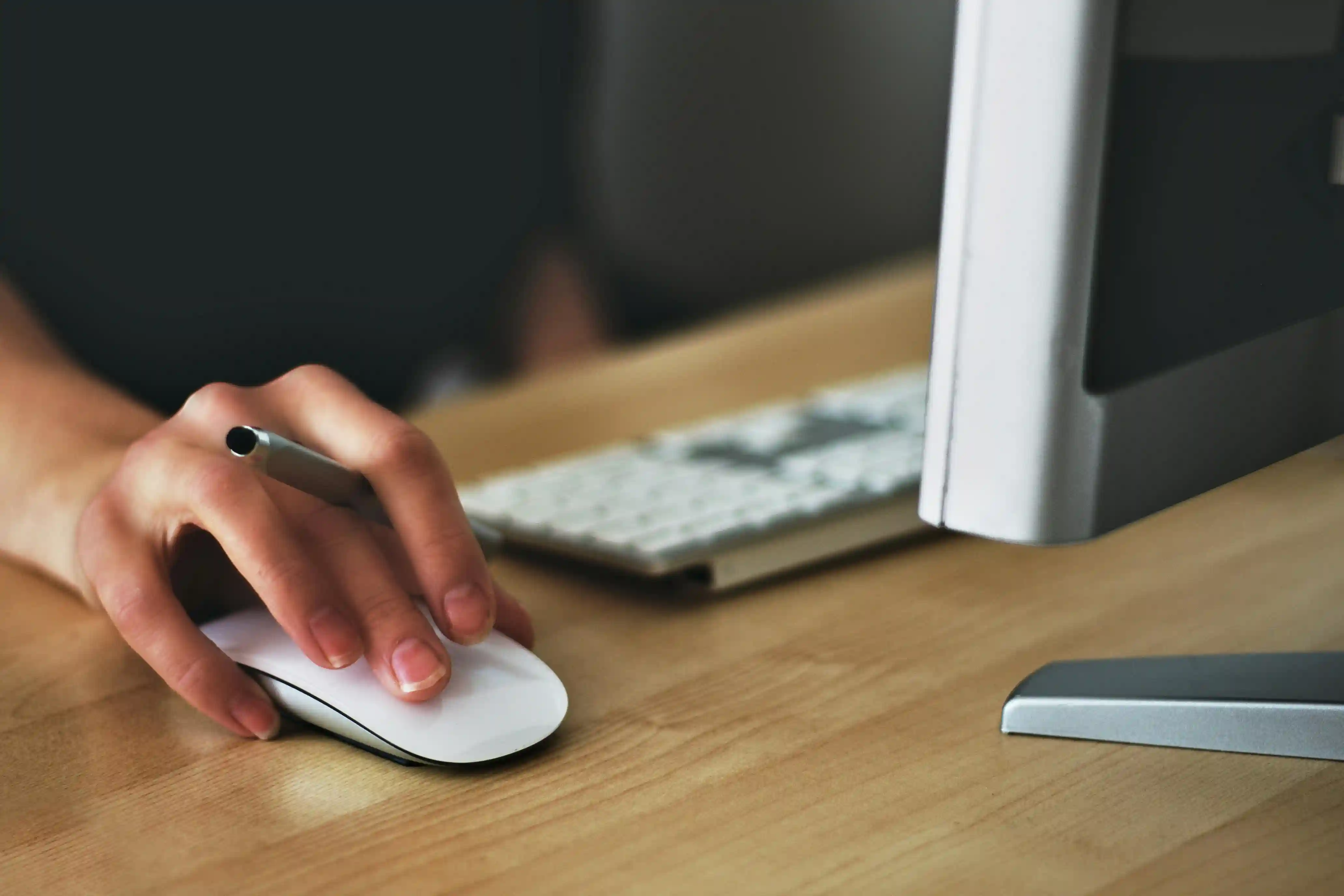Hand using a computer mouse next to a keyboard and monitor.