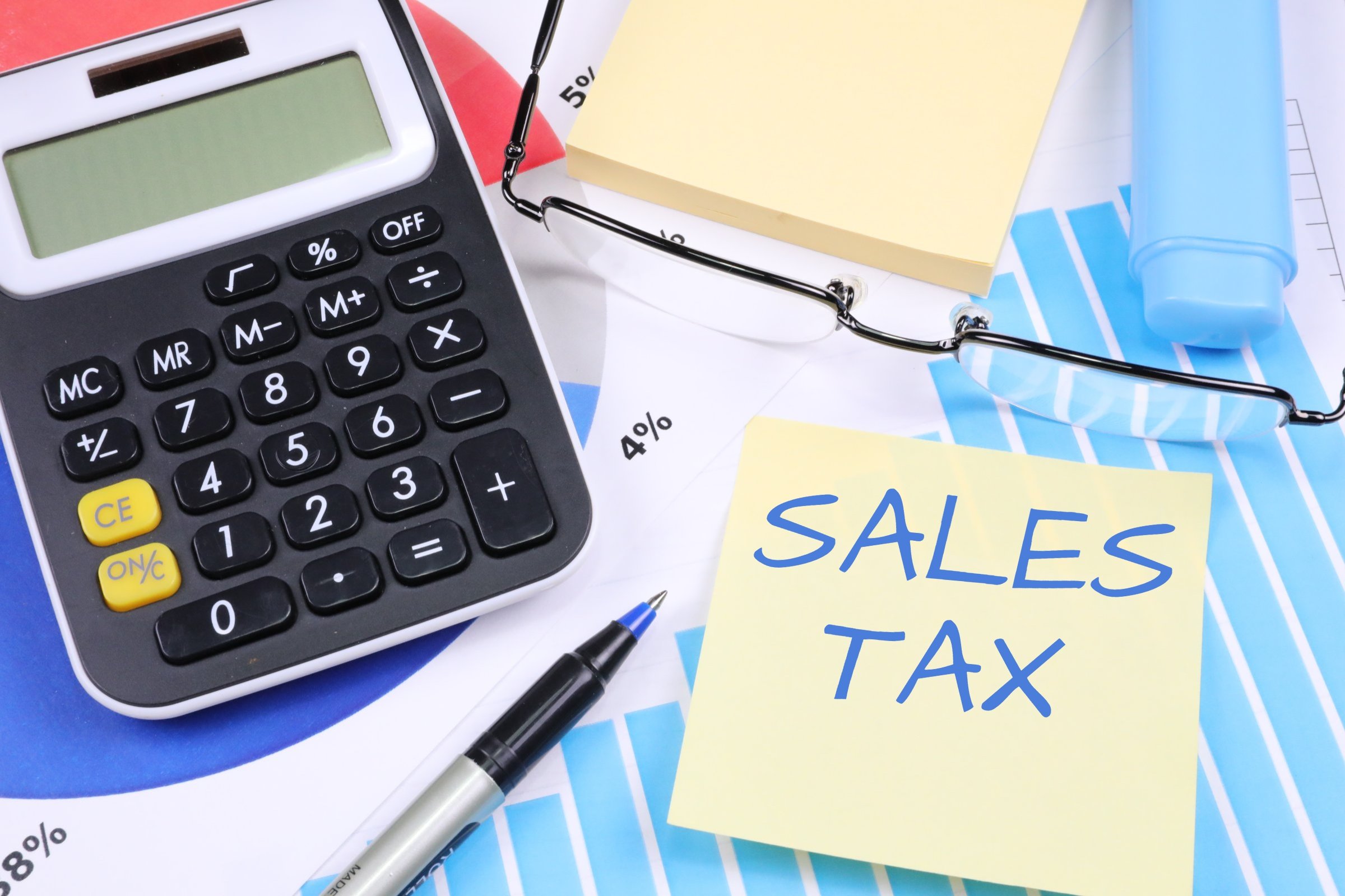 Calculator, glasses, and a “SALES TAX” sticky note on top of financial charts.
