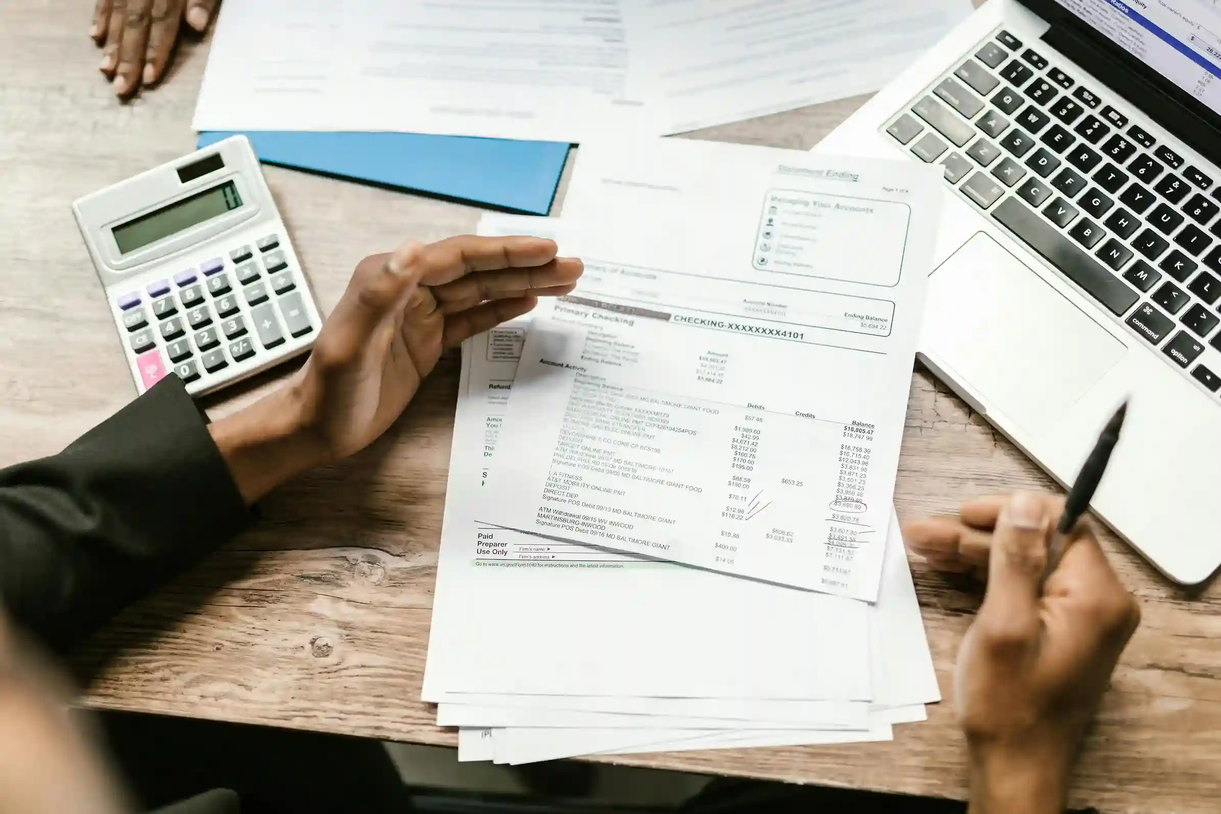 Person reviewing financial documents with a calculator and laptop on a desk.