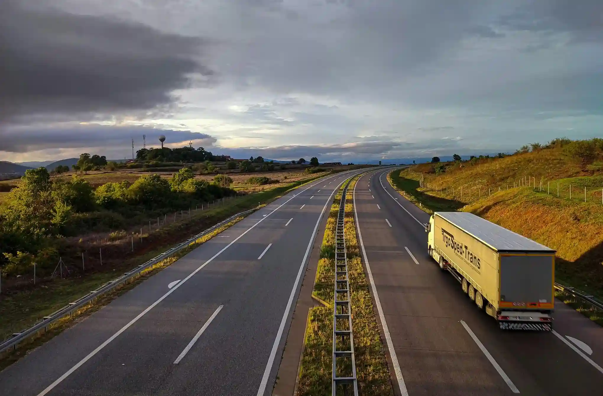 Truck driving on an empty highway at sunset.
