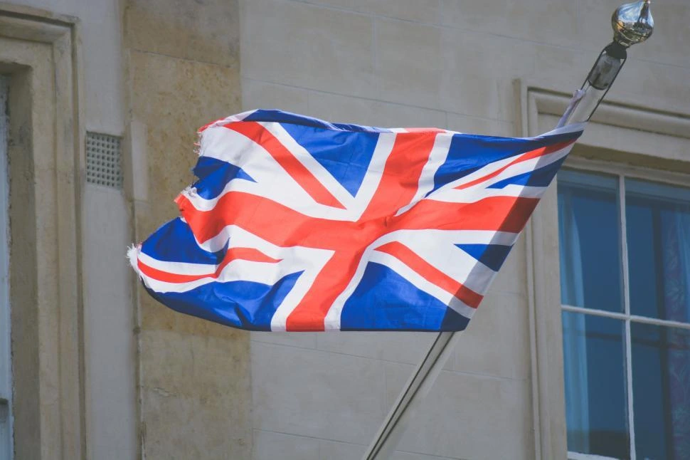 Union Jack flag waving on a pole outside a stone building in the UK.