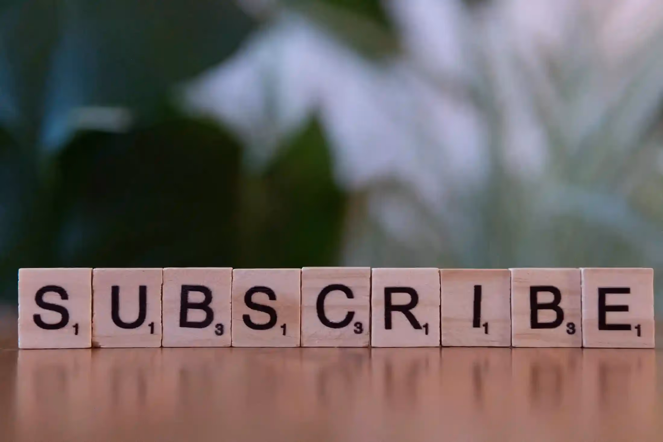Scrabble tiles spelling 'SUBSCRIBE' on a wooden surface, symbolising subscription-based business models and recurring revenue.