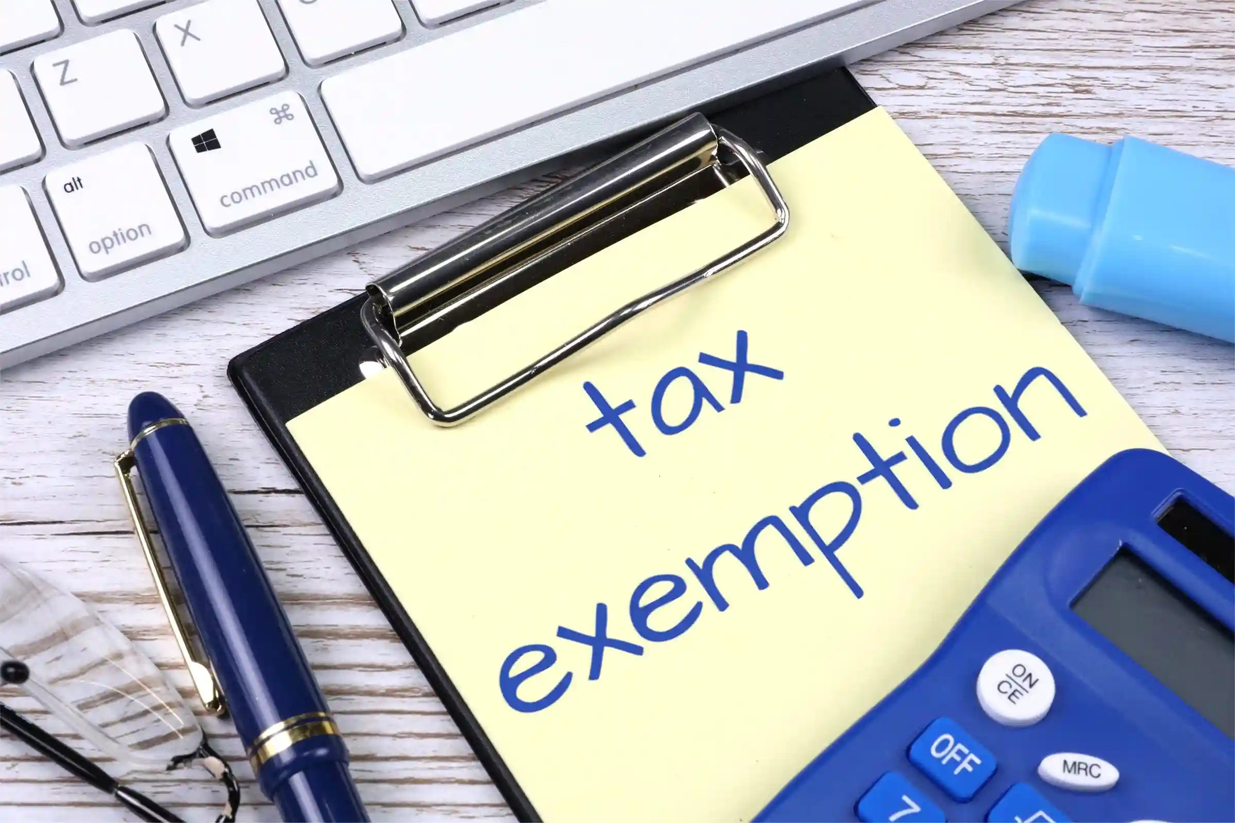 Tax exemption written on clipboard, with calculator, pen, and keyboard on desk – representing sales tax exemptions for businesses.