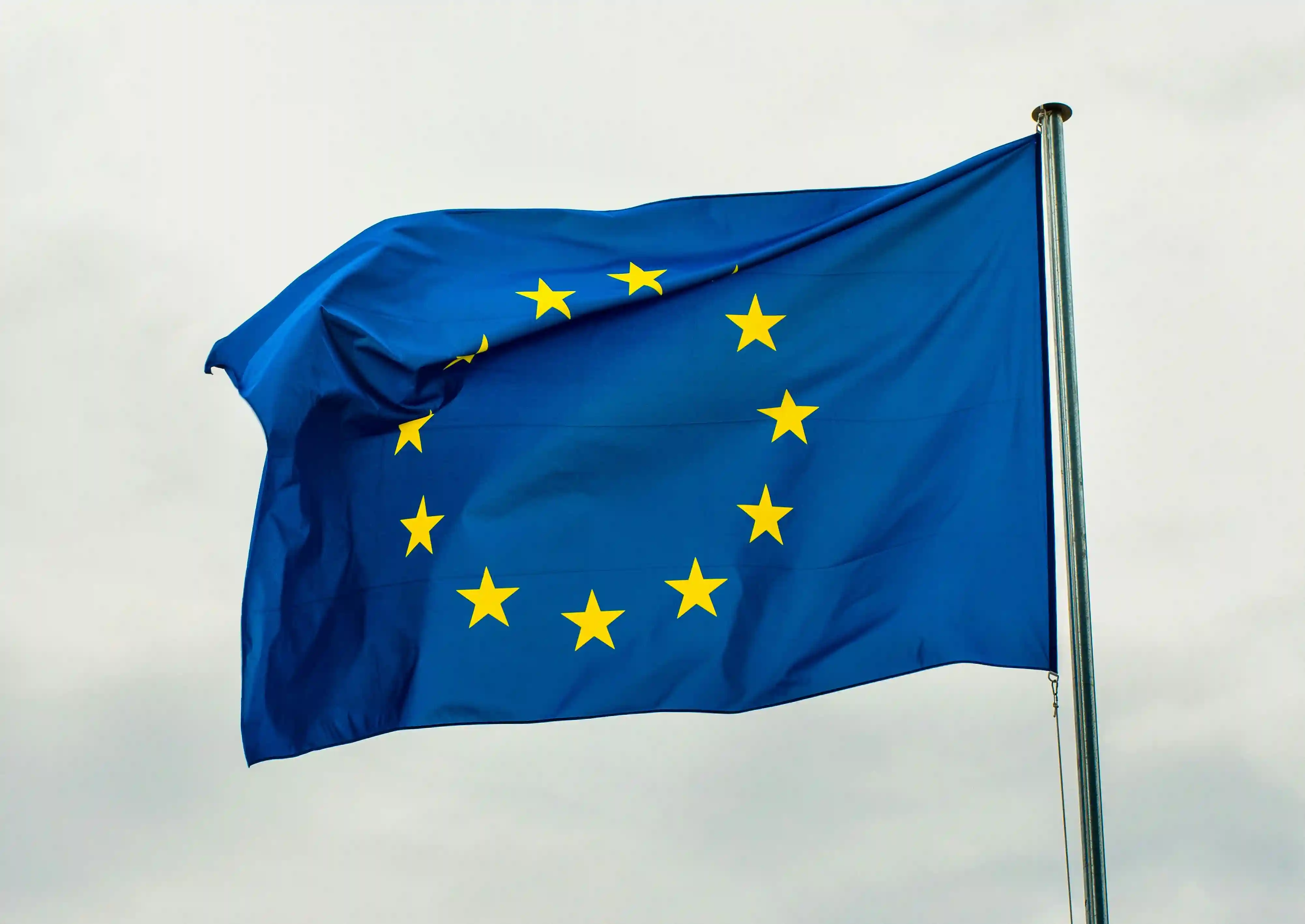 The European Union flag waving, showing a circle of yellow stars on a blue background.