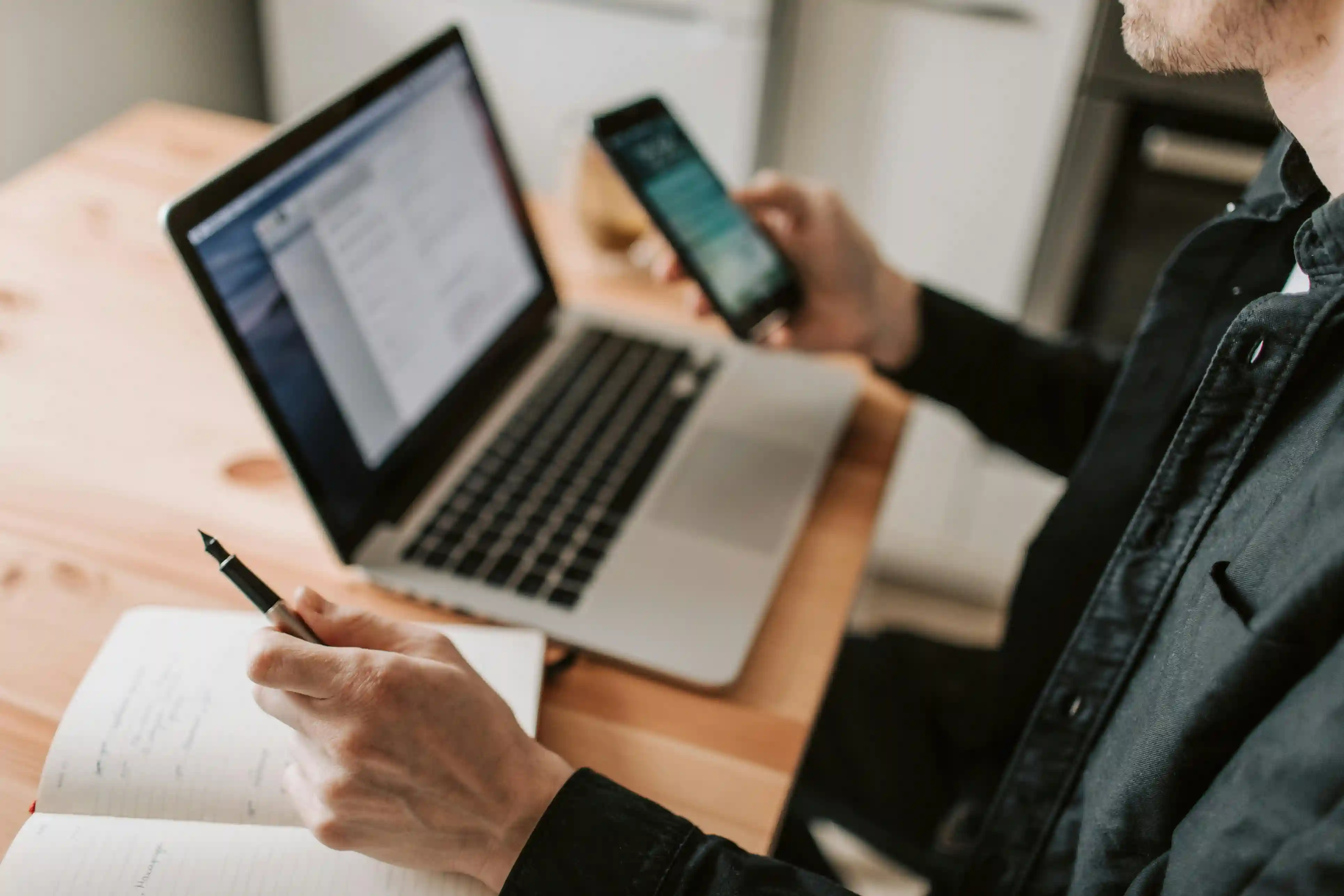 Person working at a desk with a laptop, phone, and notebook.