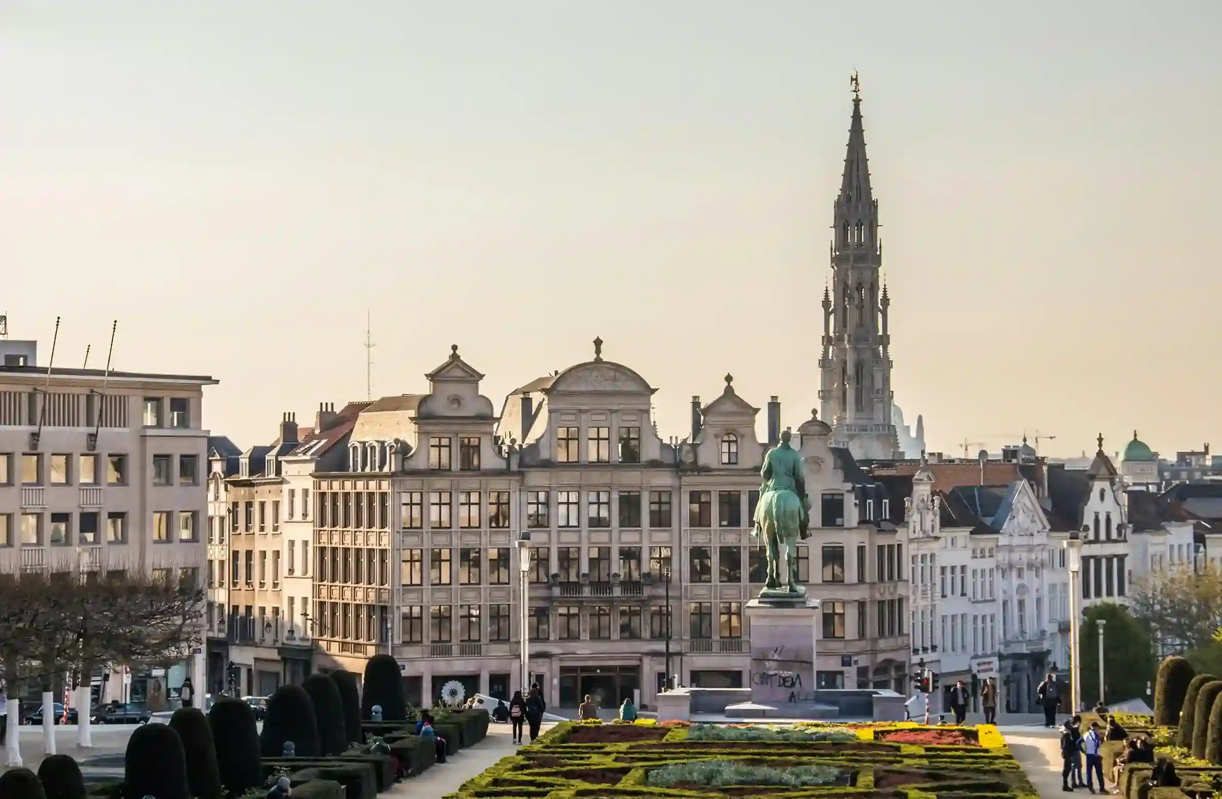 Garden view in Brussels with an equestrian statue and the Town Hall spire in the background.