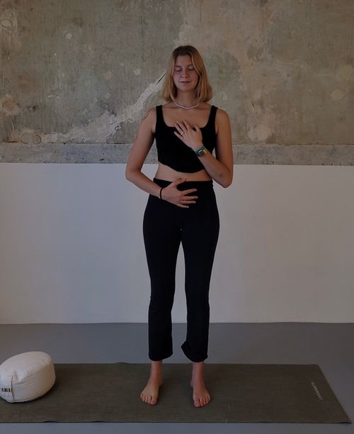 Milli in Mountain Pose with her hands on belly and chest.