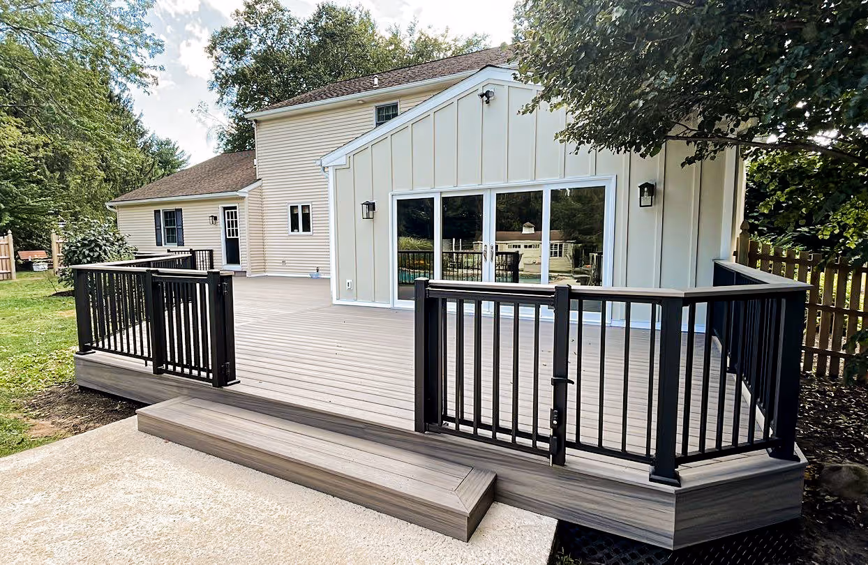 Newly constructed residential deck with composite flooring and black railing, attached to a white siding house.