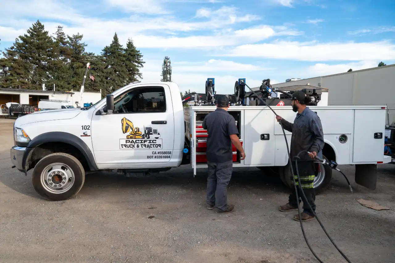 Service truck marked “Pacific Truck & Tractor”; two techs deploy fuel hose and open tool drawer for field repairs.