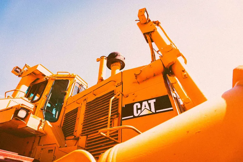 Yellow Caterpillar bulldozer with CAT logo under bright sunlight, showing cab and hydraulic components.