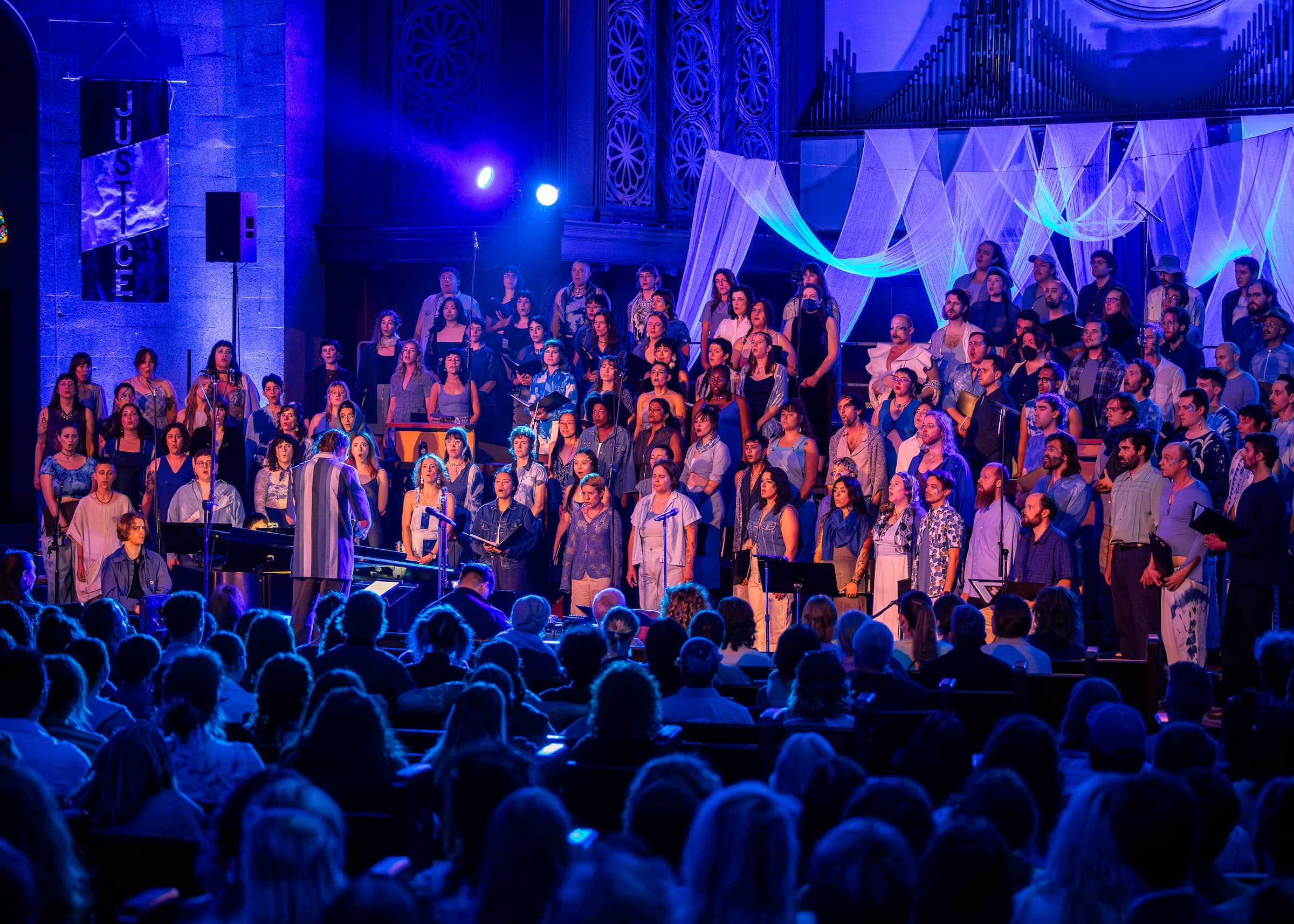 120+ choir members on stage, lit in blue, focused on choir Director Derek Sup.