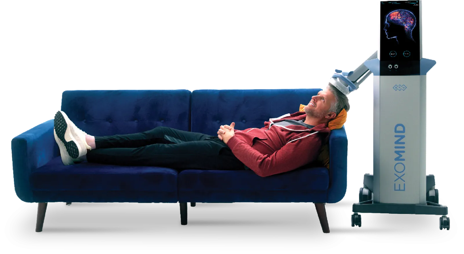 Man lying on a blue sofa with a white brain stimulation device on his head connected to a machine labeled EXOMIND.