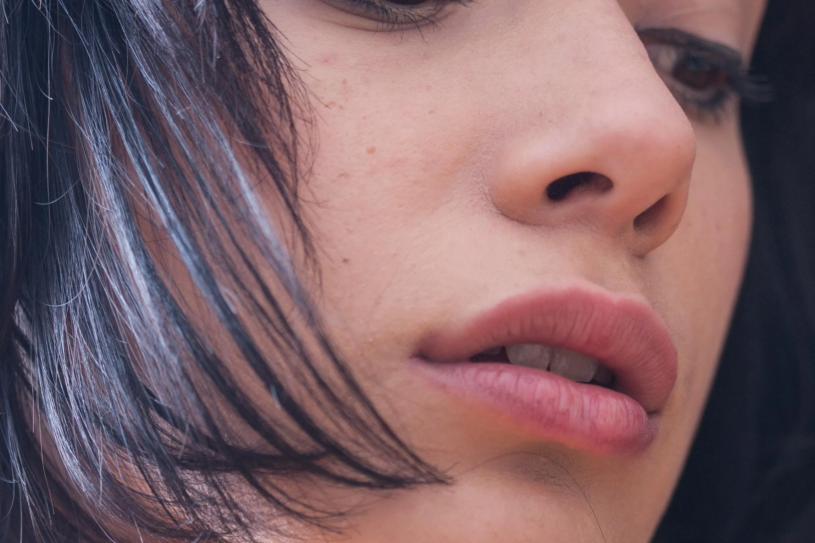Close-up of a person's lips, nose, and part of the face with black hair partially covering the cheek.