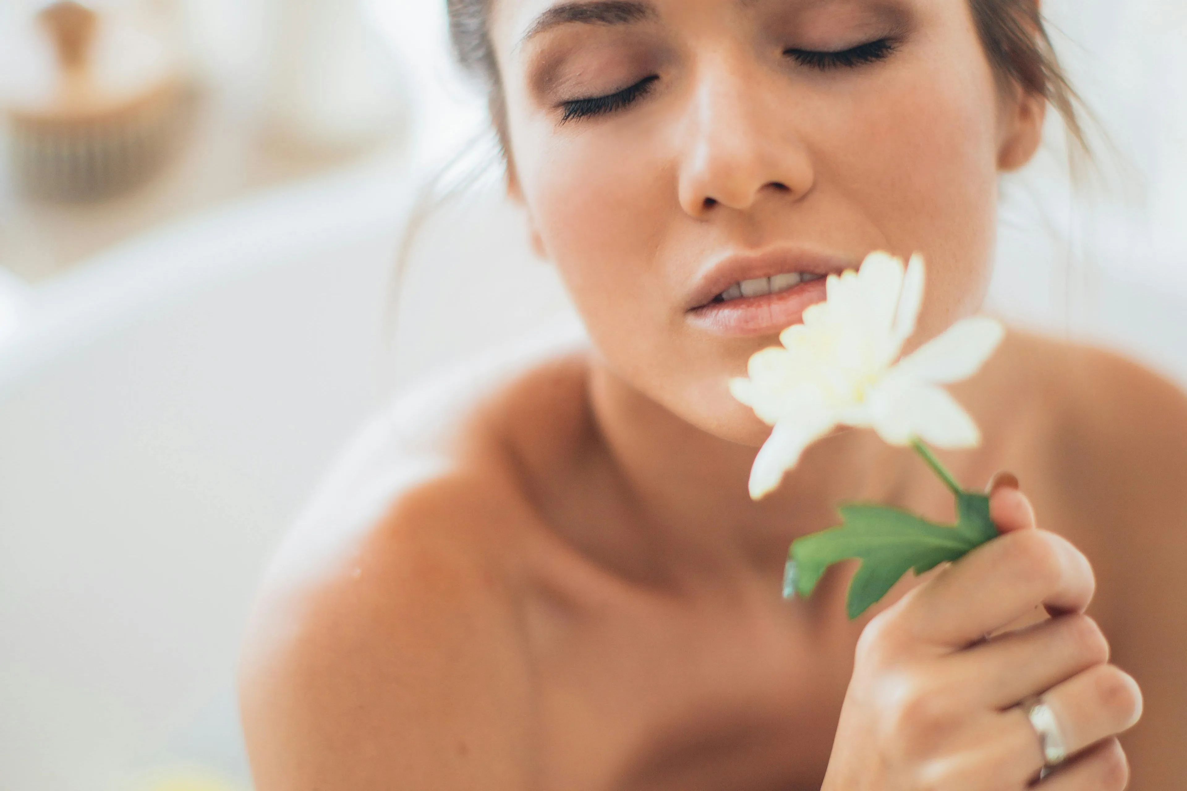 Close-up of a woman with closed eyes gently holding a white flower near her face.