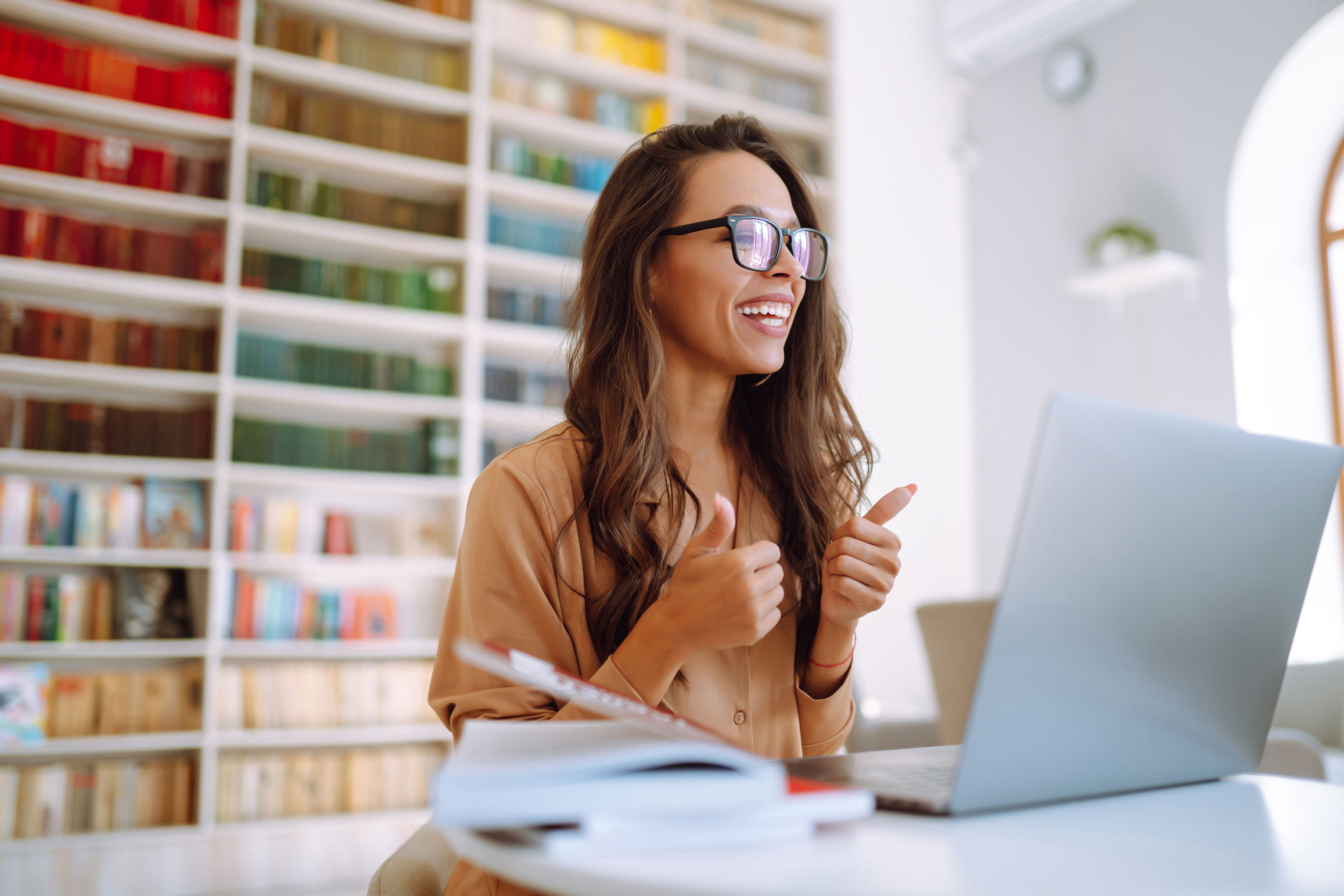 Smiling property manager with glasses giving a thumbs-up at her laptop while reviewing tenant applications