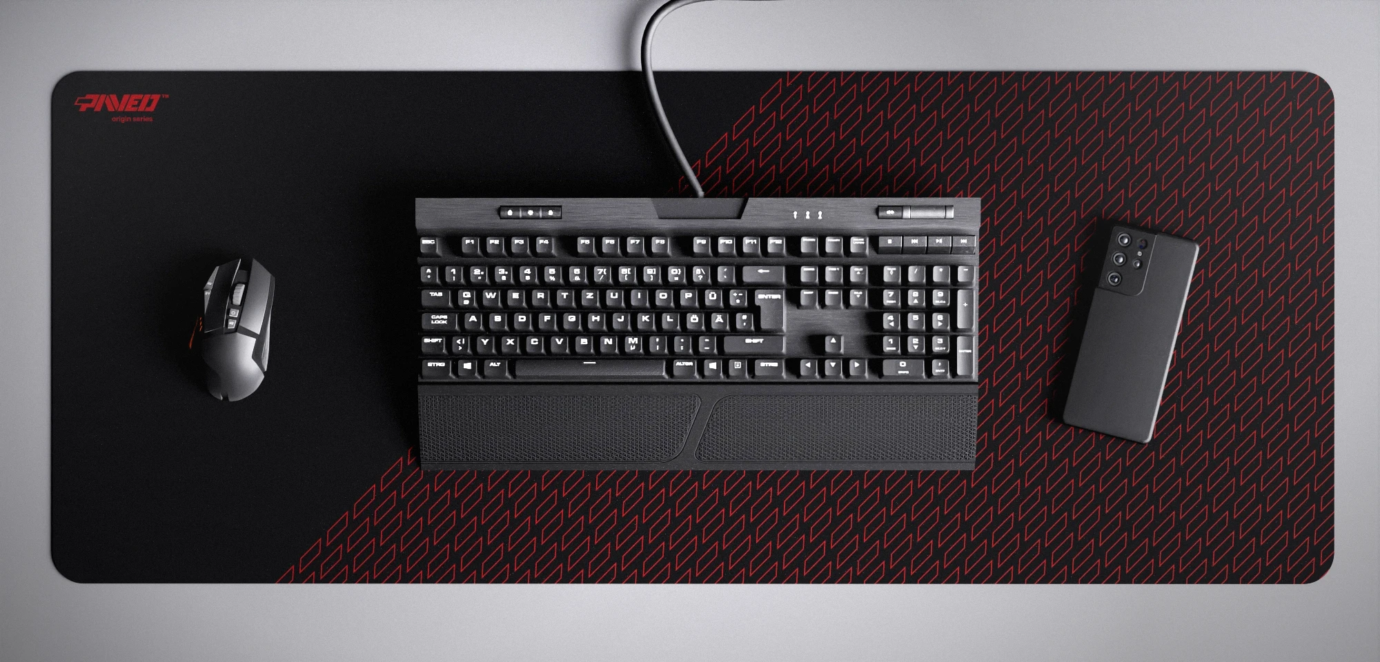 Top view of Night Imperial Pathfinder XXL deskmat 1000mm x 400mm left-handed variant featuring geometric tiled pattern in red and black, water-resistant antimicrobial polyester surface, shown with full-size mechanical keyboard, gaming mouse, and smartphone for scale, ultra-lightweight odour-free AreoFlex microruber base, stitch-free professional finish.