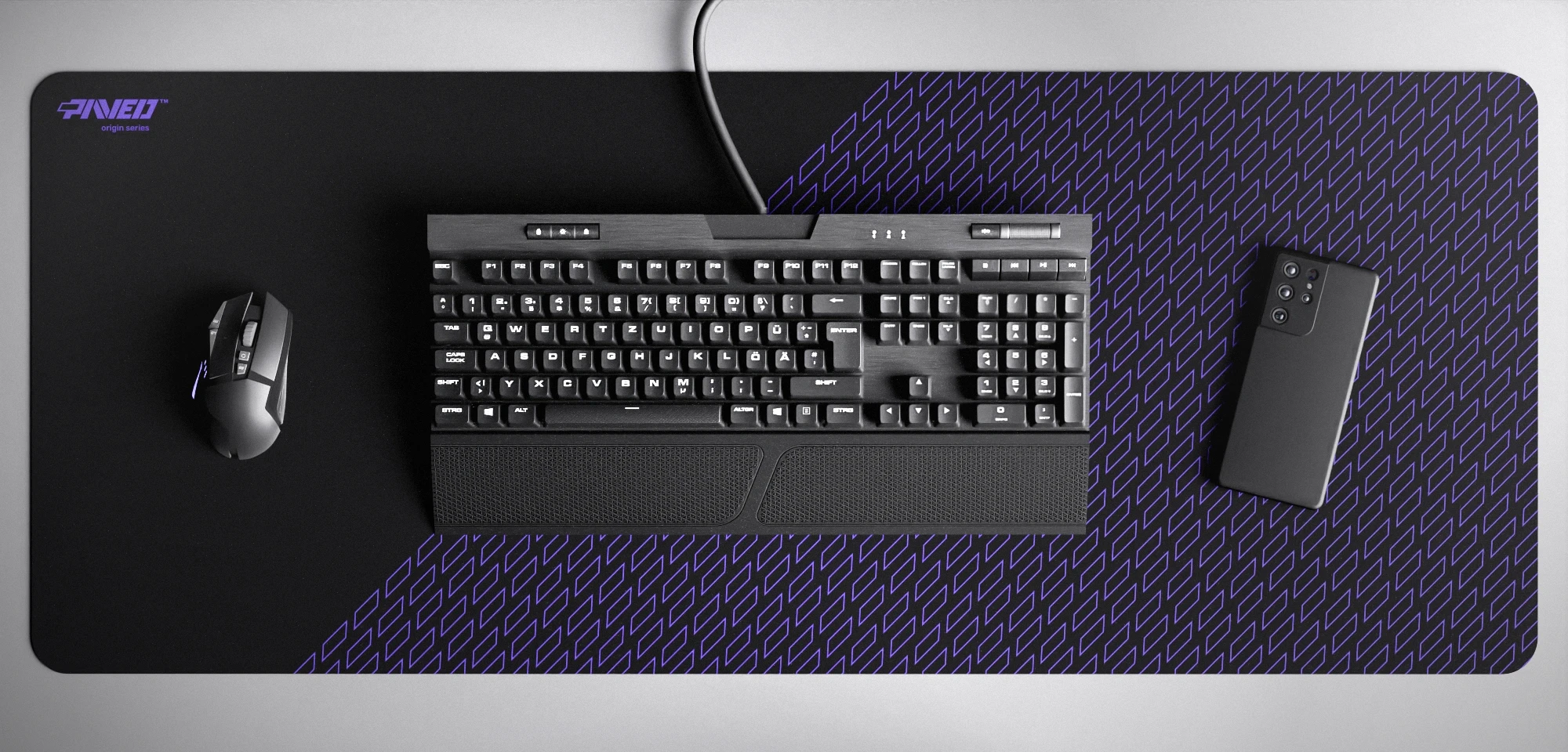 Top view of Night Amethyst Pathfinder XXL deskmat 1000mm x 400mm left-handed variant featuring geometric tiled pattern in purple and black, water-resistant antimicrobial polyester surface, shown with full-size mechanical keyboard, gaming mouse, and smartphone for scale, ultra-lightweight odour-free AreoFlex microruber base, stitch-free professional finish.