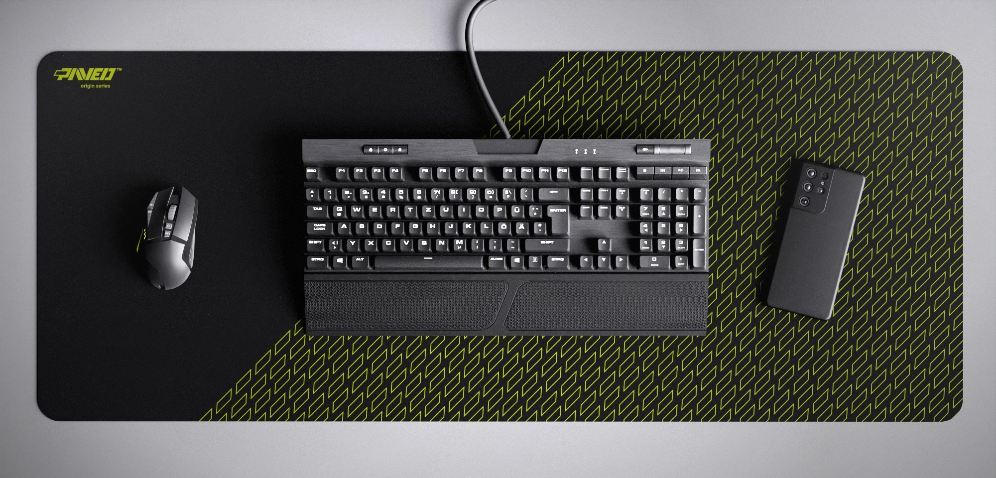 Top view of Night Toxic Pathfinder XXL deskmat 1000mm x 400mm left-handed variant featuring geometric tiled pattern in light green and black, water-resistant antimicrobial polyester surface, shown with full-size mechanical keyboard, gaming mouse, and smartphone for scale, ultra-lightweight odour-free AreoFlex microruber base, stitch-free professional finish.