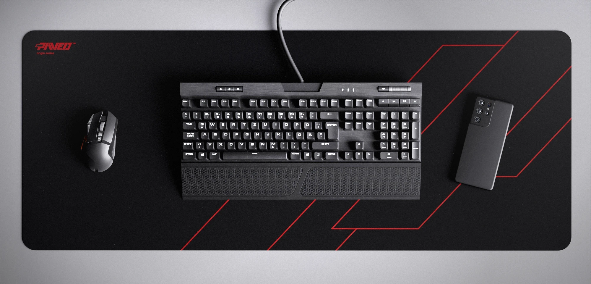 Top view of Night Imperial Formula XXL deskmat 1000mm x 400mm left-handed variant featuring geometric angular line pattern in red and black, water-resistant antimicrobial polyester surface, shown with full-size mechanical keyboard, gaming mouse, and smartphone for scale, ultra-lightweight odour-free AreoFlex microruber base, stitch-free professional finish.