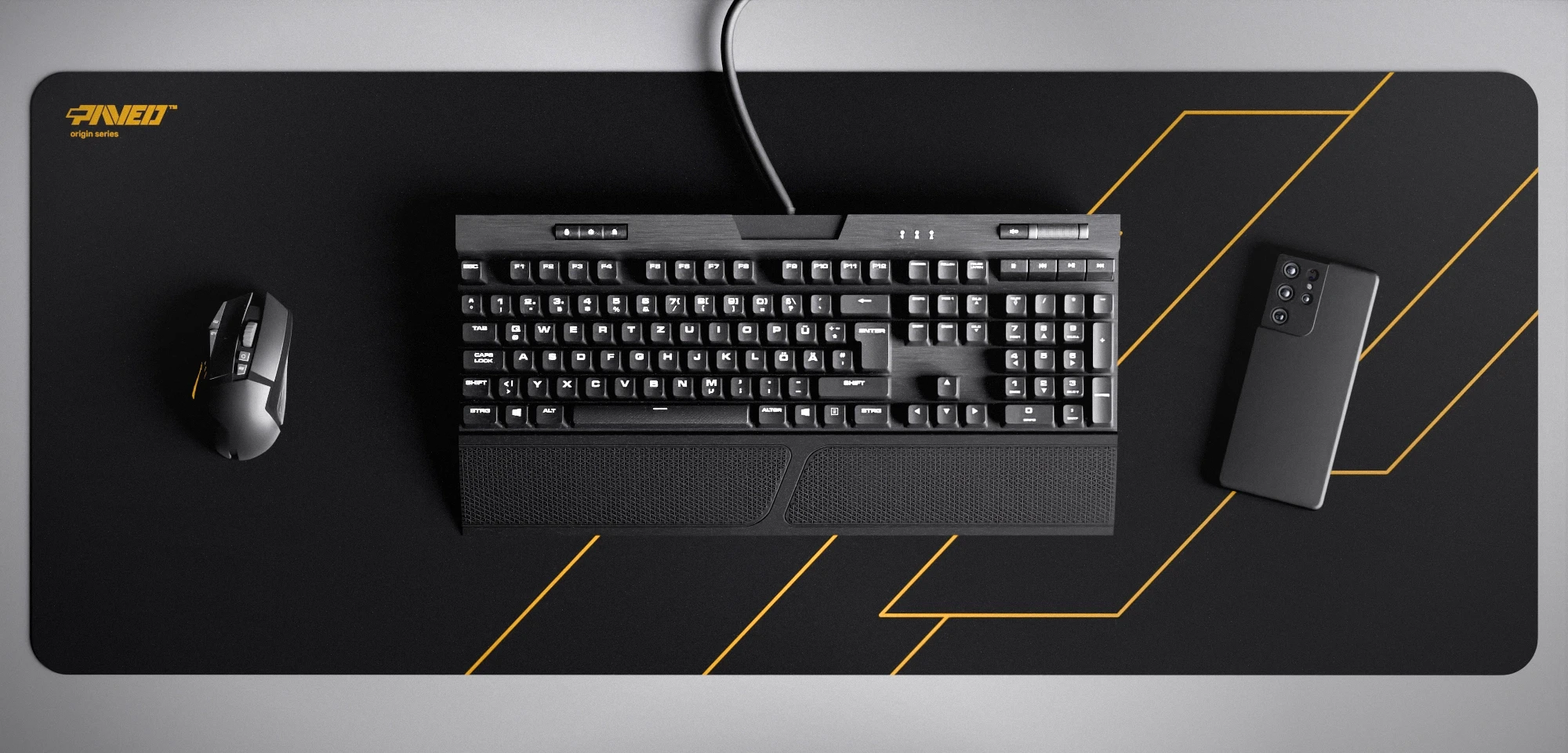 Top view of Night Desert Formula XXL deskmat 1000mm x 400mm left-handed variant featuring geometric angular line pattern in deep yellow and black, water-resistant antimicrobial polyester surface, shown with full-size mechanical keyboard, gaming mouse, and smartphone for scale, ultra-lightweight odour-free AreoFlex microruber base, stitch-free professional finish.